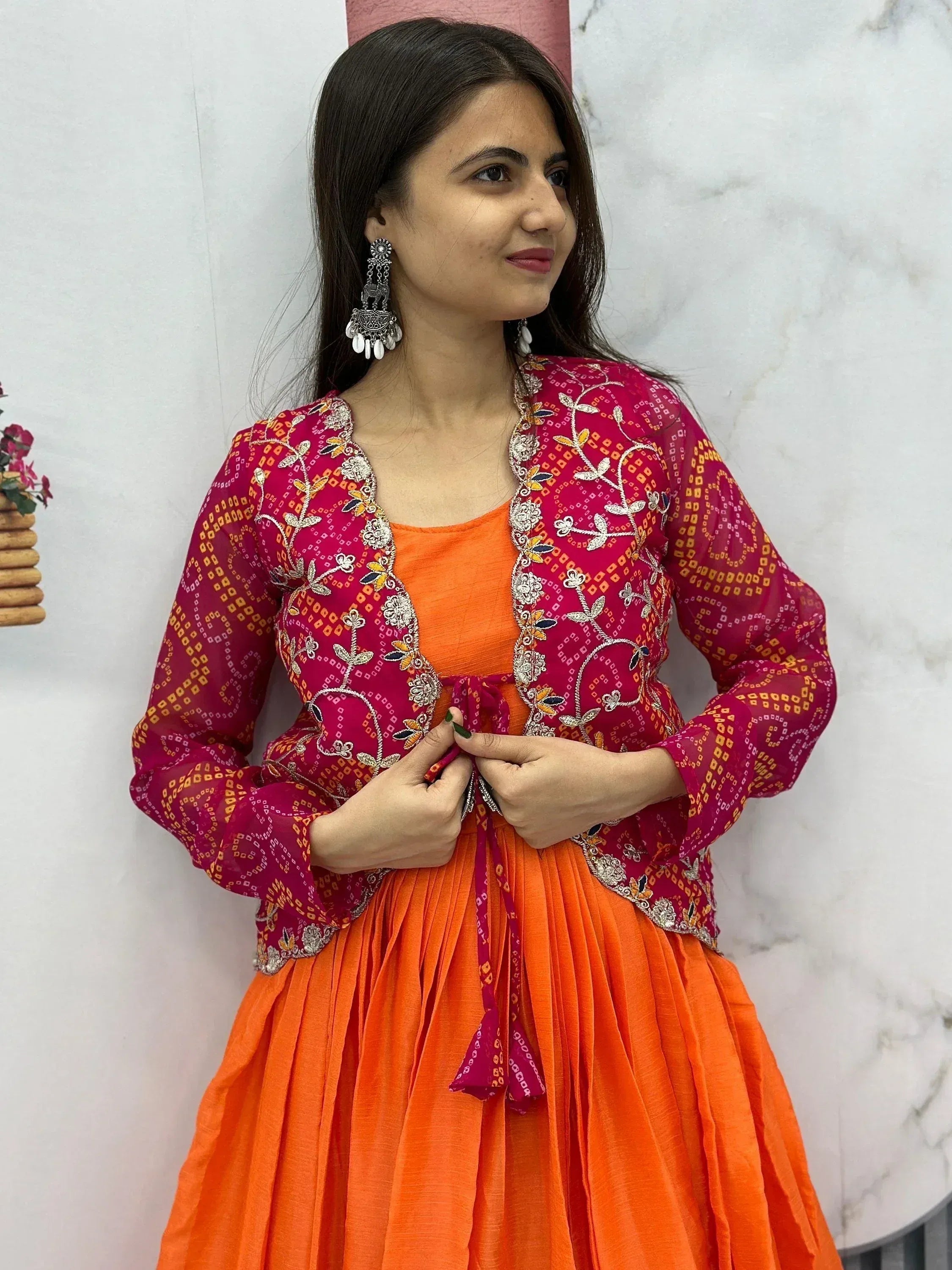 Woman in vibrant orange ethnic gown with embroidered magenta jacket, perfect for festive occasions.