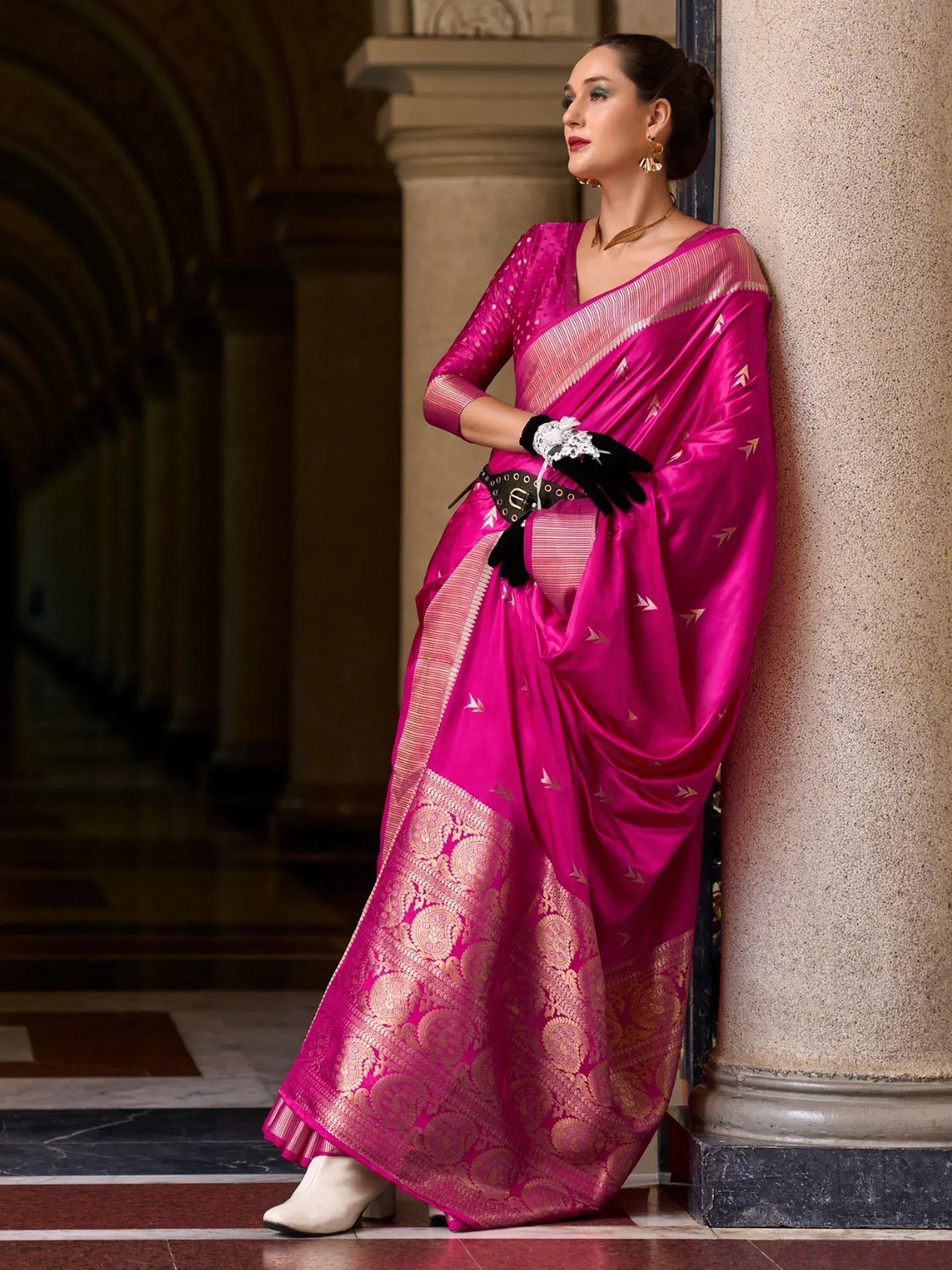 Woman in vibrant pink silk saree with gold paisley border, styled with gloves and belt for ethnic fashion