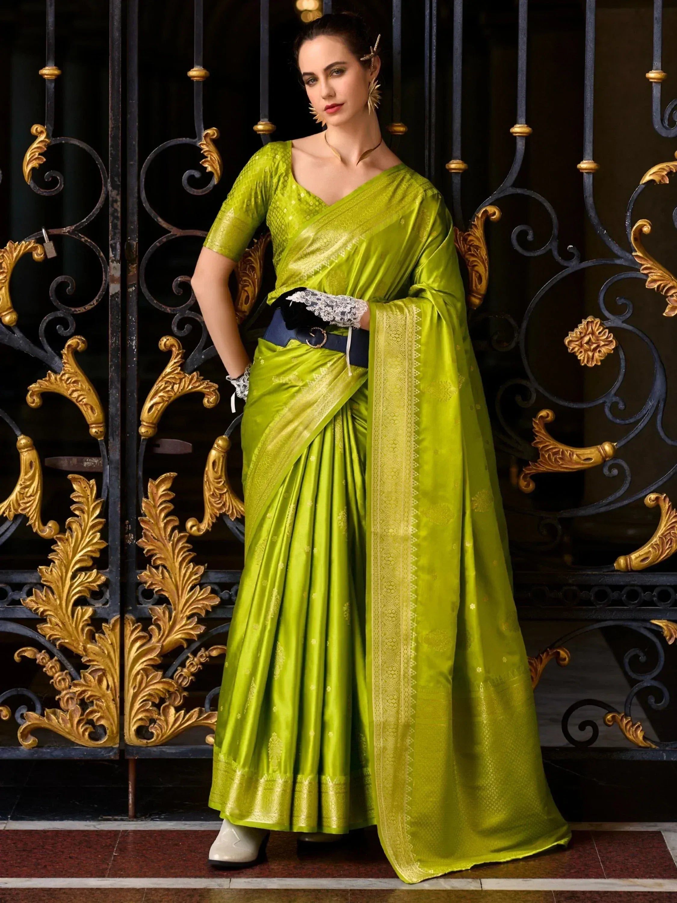 Vibrant green designer saree with gold border, paired with lace gloves and statement earrings, styled against ornate gate.