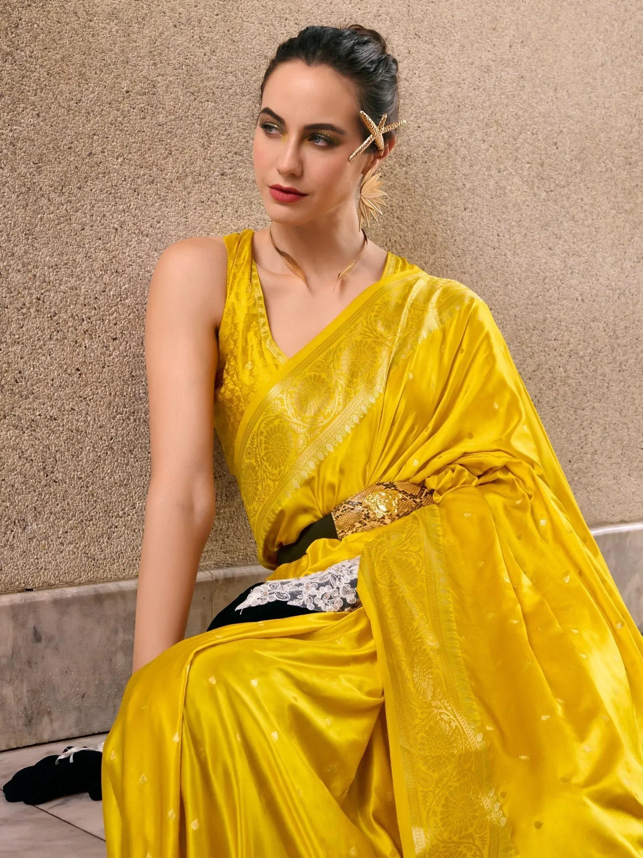 Yellow designer saree with gold embroidery, styled with statement earrings and a snake belt for ethnic wear.