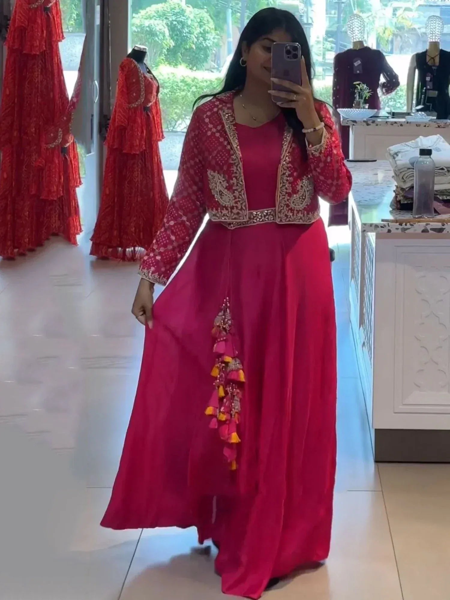 Woman in vibrant pink ethnic gown with embroidered jacket and tassel details, perfect for Indian occasions.