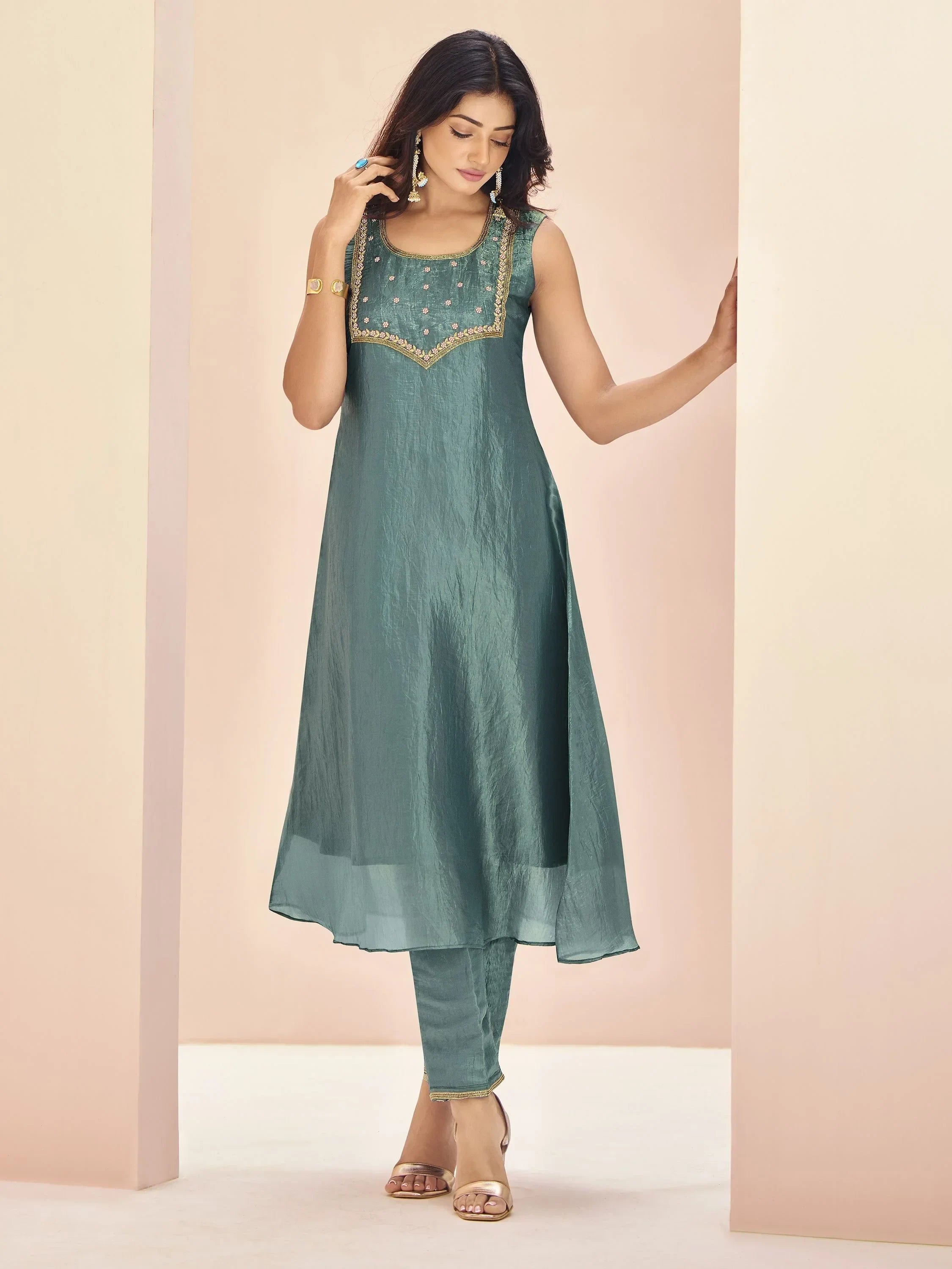 Woman wearing teal green sleeveless kurti with gold embellishments and matching pants