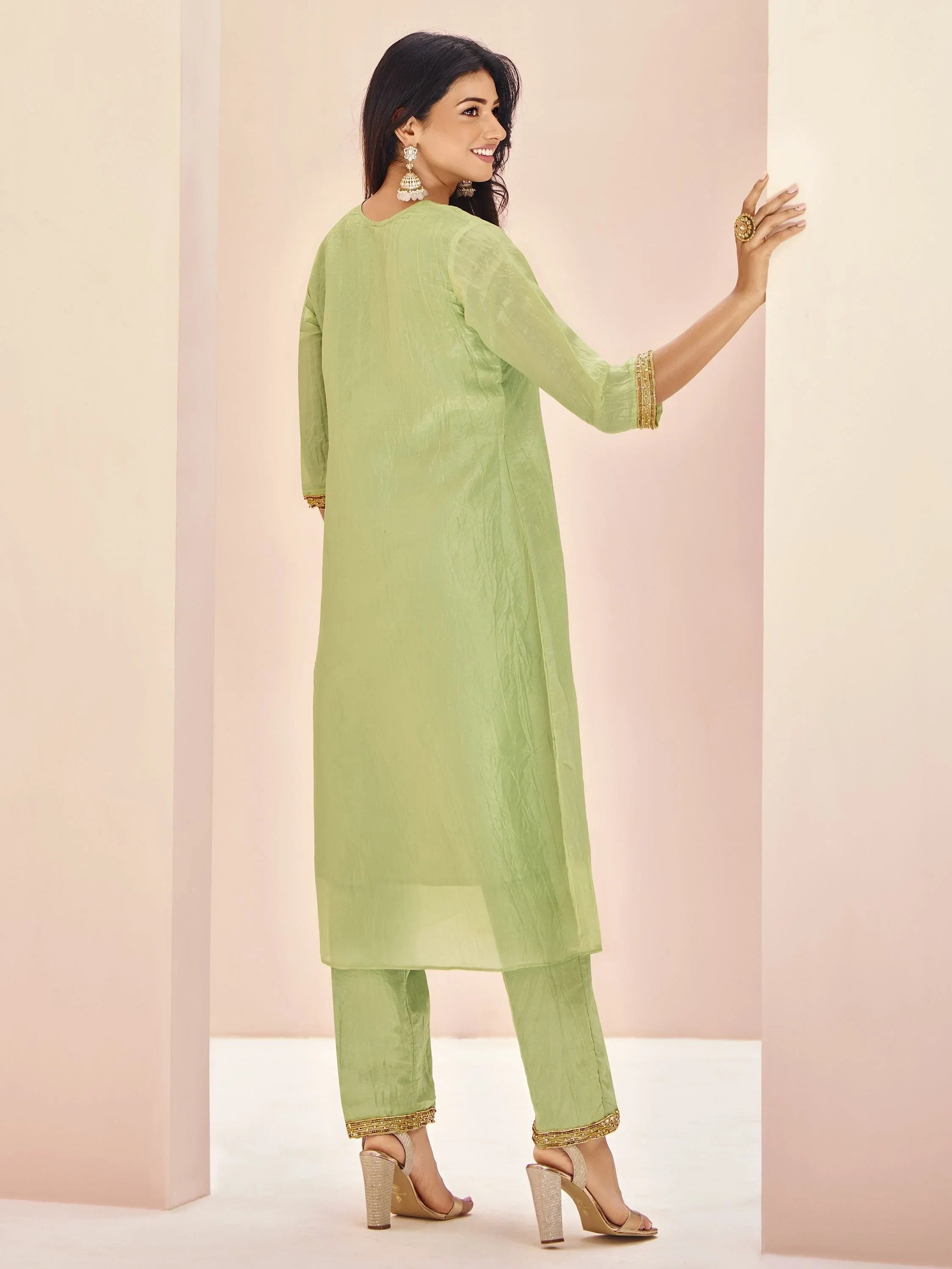 Woman in light green straight-cut salwar kameez with gold heels and statement earrings