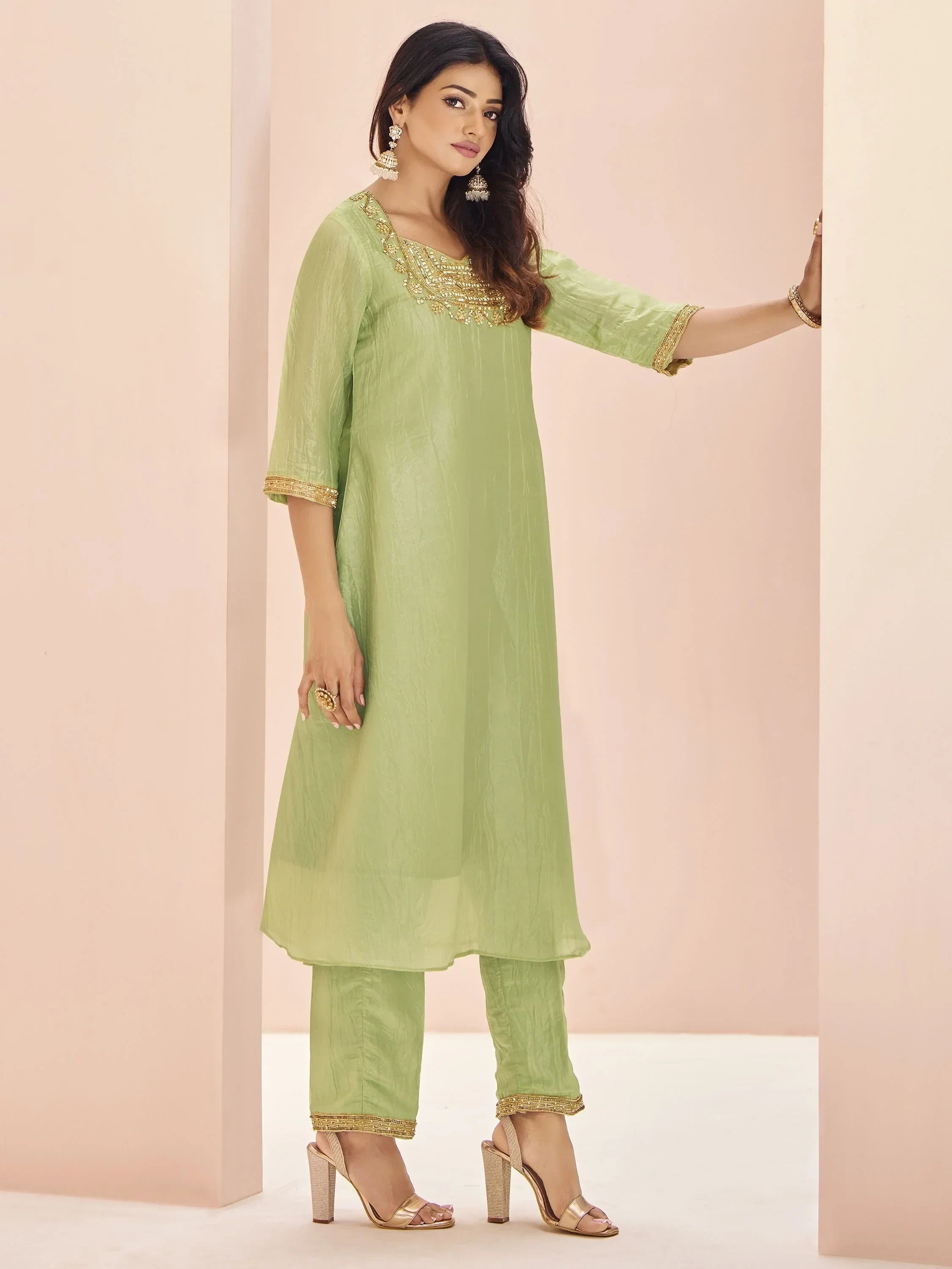 Woman wearing a light green embroidered salwar kameez with gold accents and heels