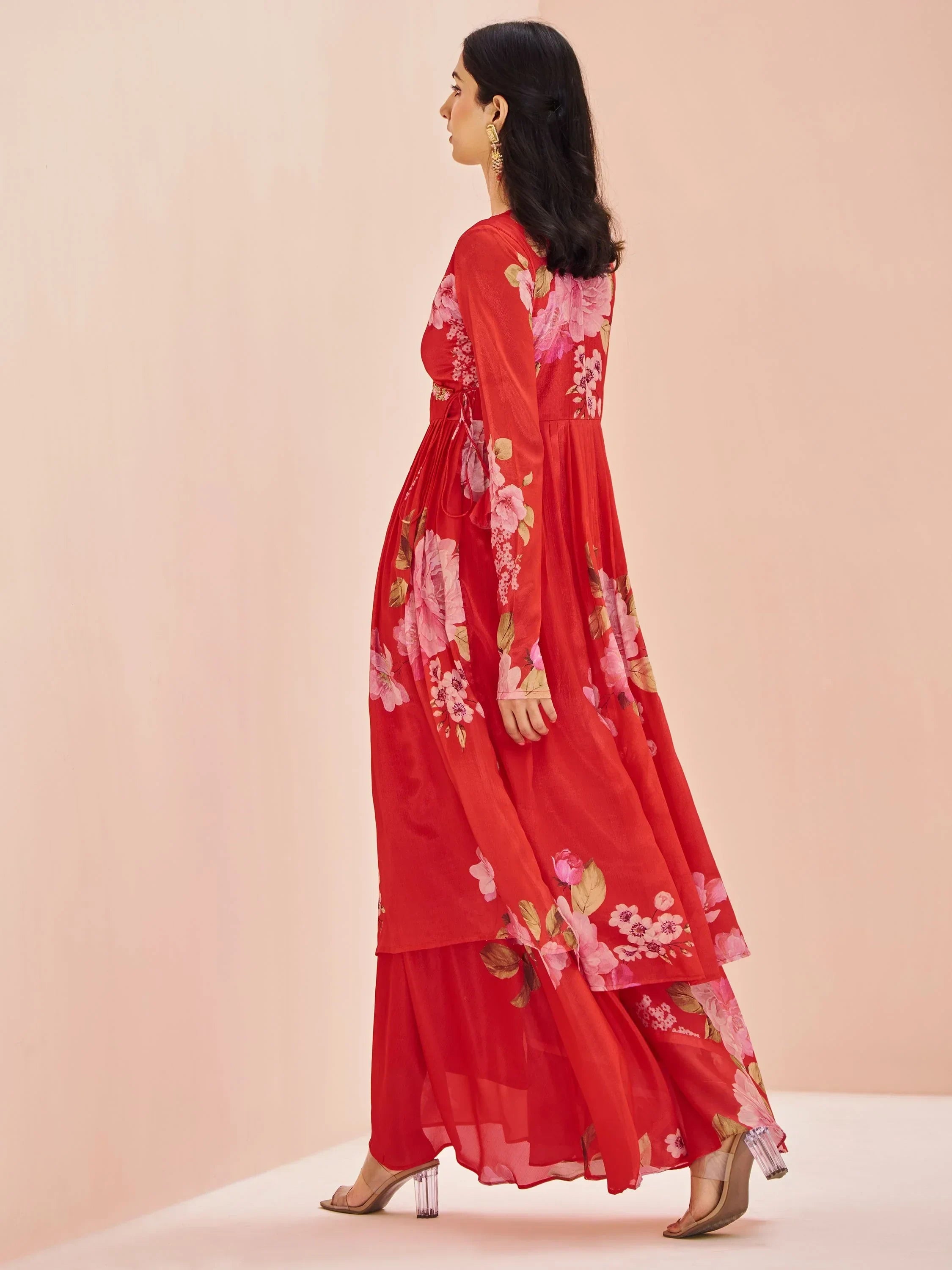 Woman in red floral ethnic gown with sheer sleeves and flowy skirt, side view