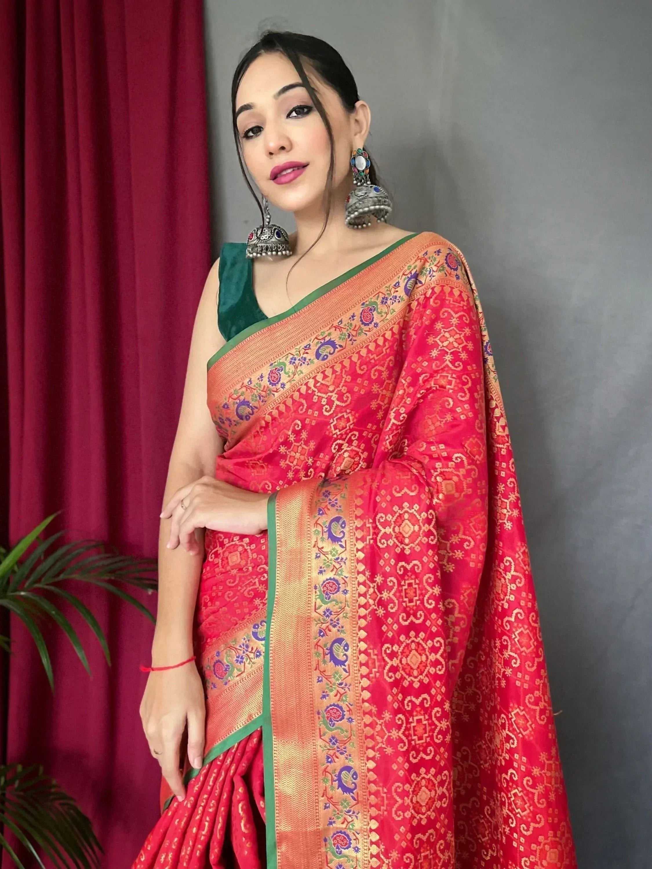 Woman in vibrant red Indian saree with gold embroidery and green blouse, styled with traditional earrings.
