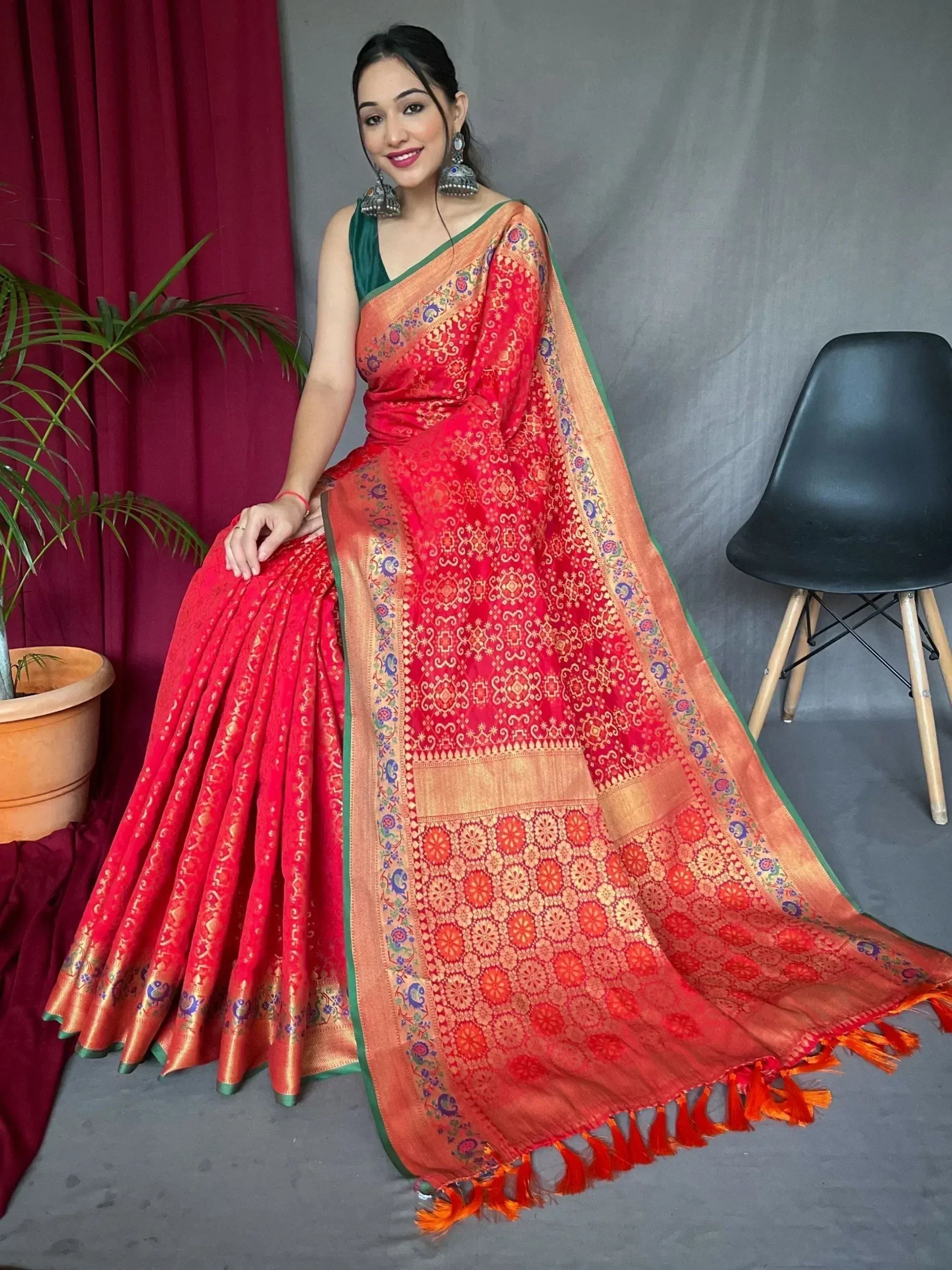 Red and gold designer saree with intricate floral patterns, green border, and tassels, paired with a green blouse.