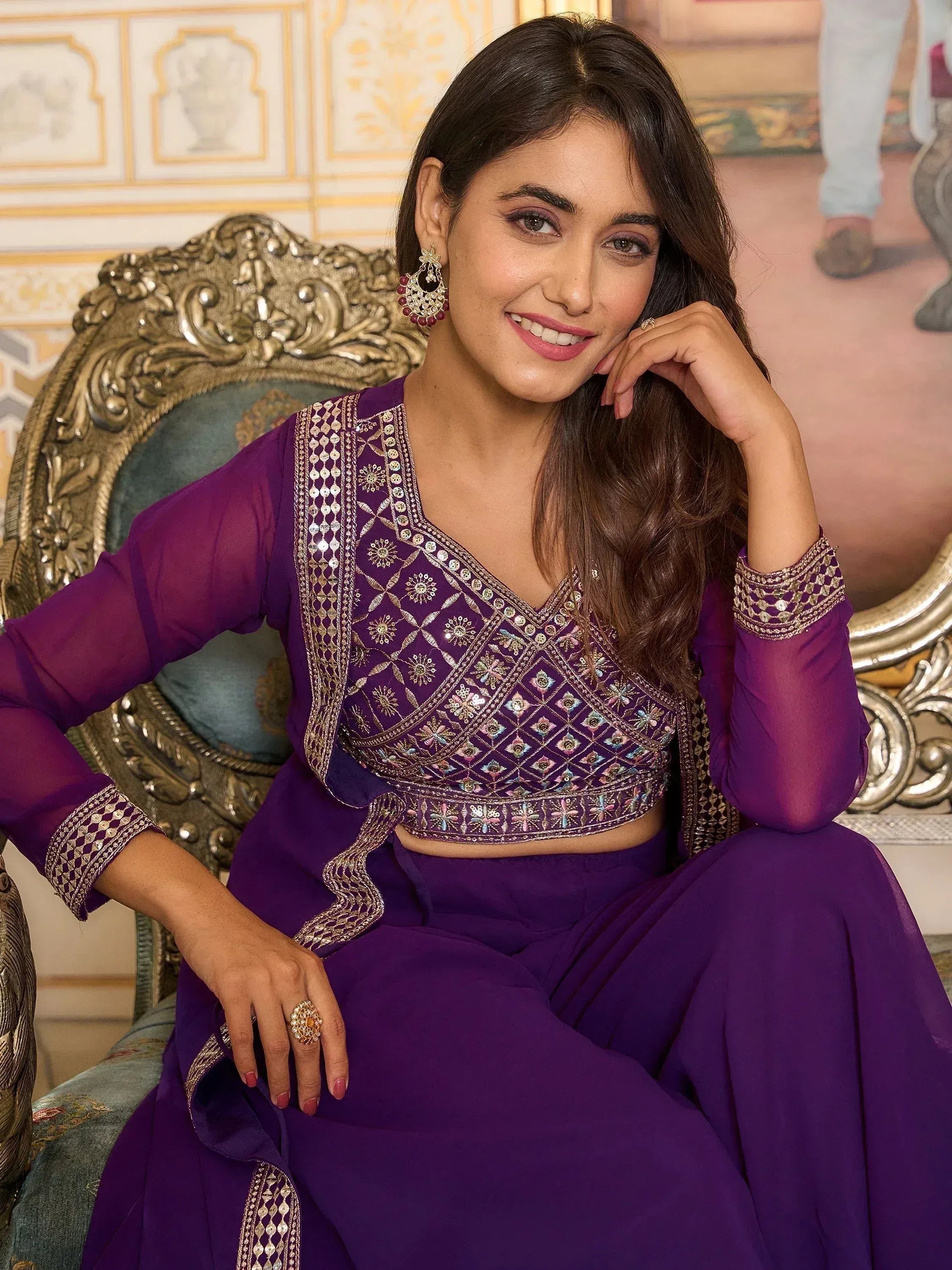 Woman in designer purple lehenga choli with mirror work, sitting on ornate chair