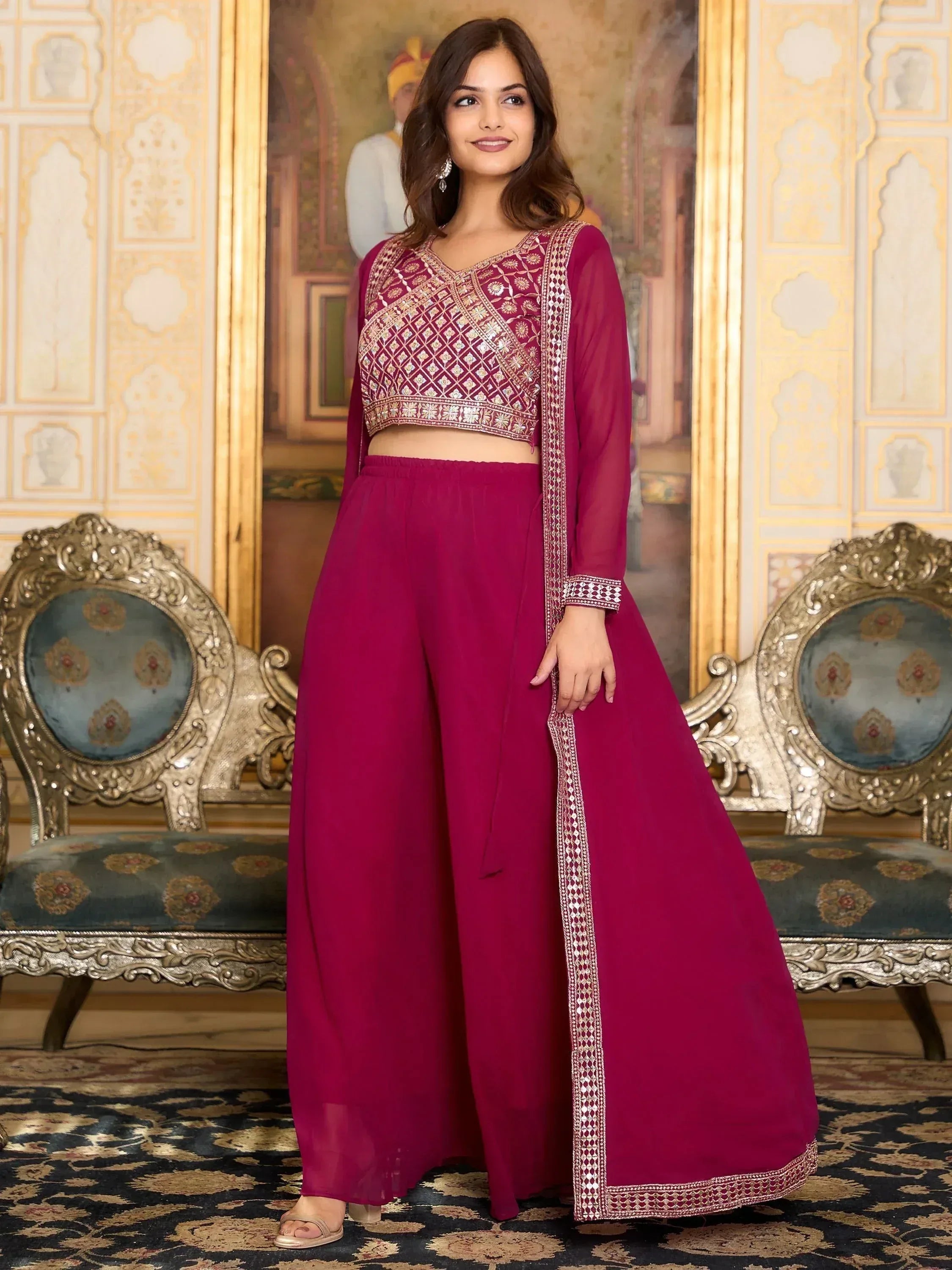 Woman in magenta embroidered lehenga choli set with dupatta, standing in ornate room