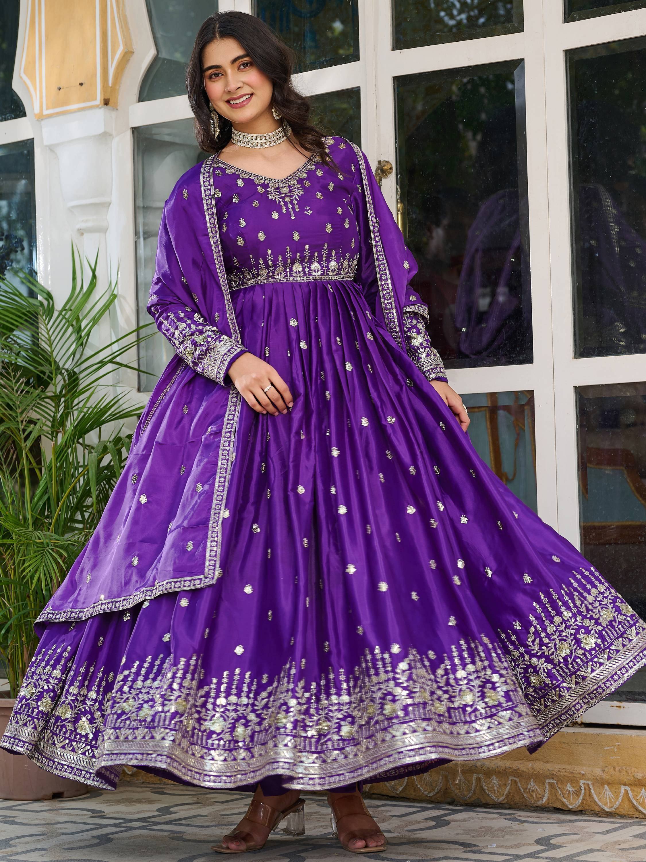 Woman wearing a purple embroidered Indian ethnic gown with dupatta, standing outdoors