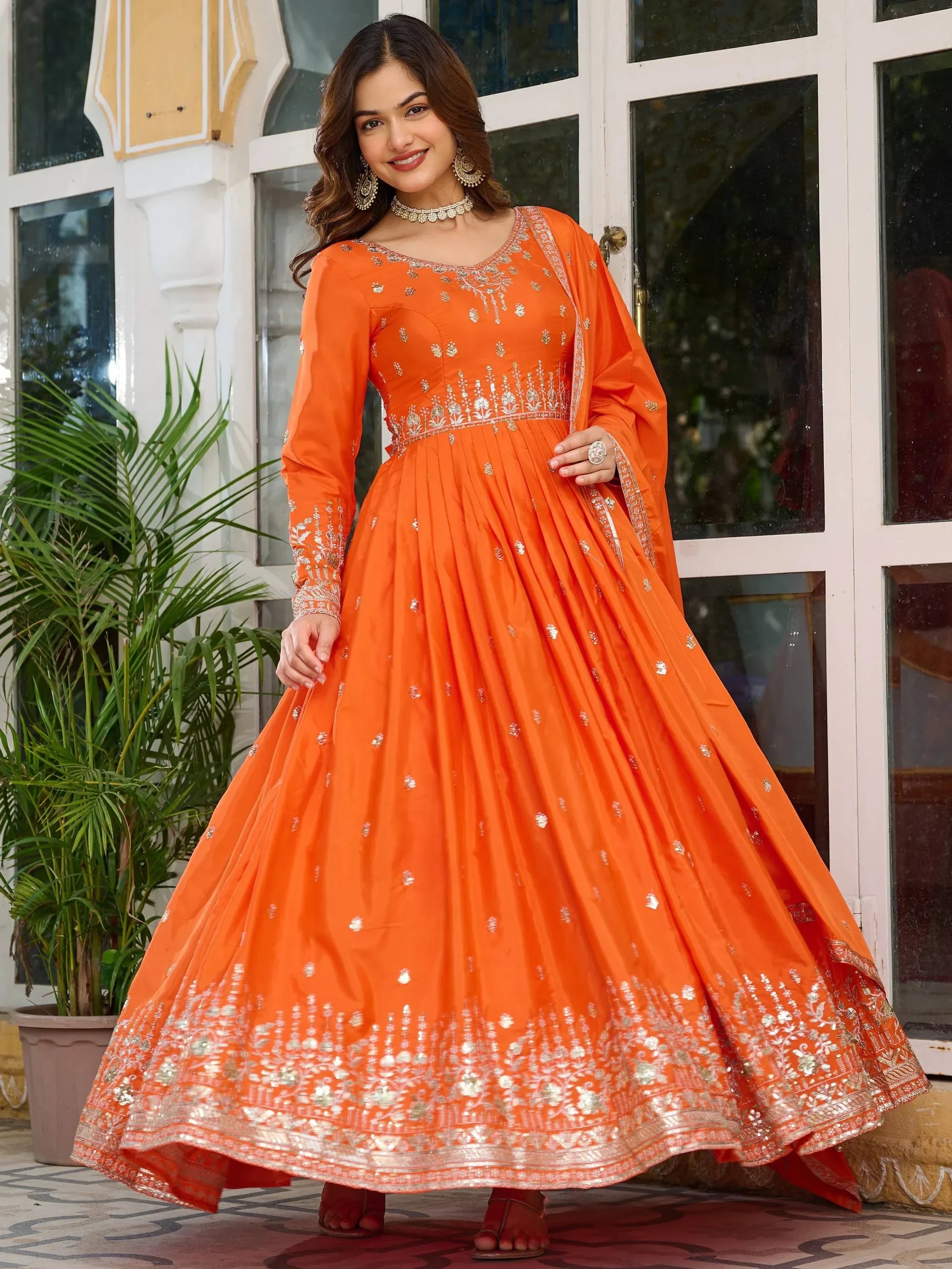Woman in vibrant orange embroidered ethnic gown with silver detailing, outdoor setting