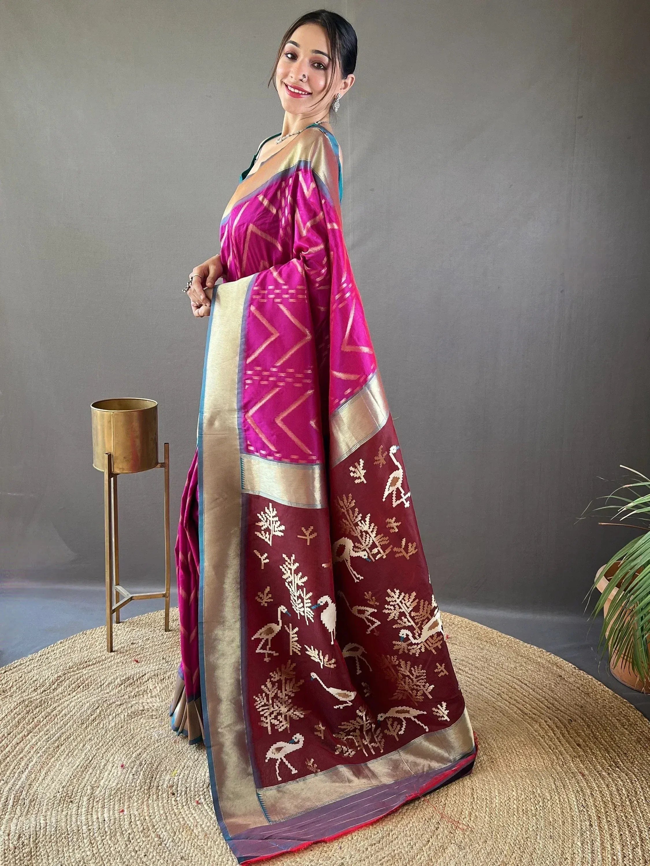Woman in vibrant pink and maroon ethnic saree with bird and tree motifs, gold border, designer Indian wear