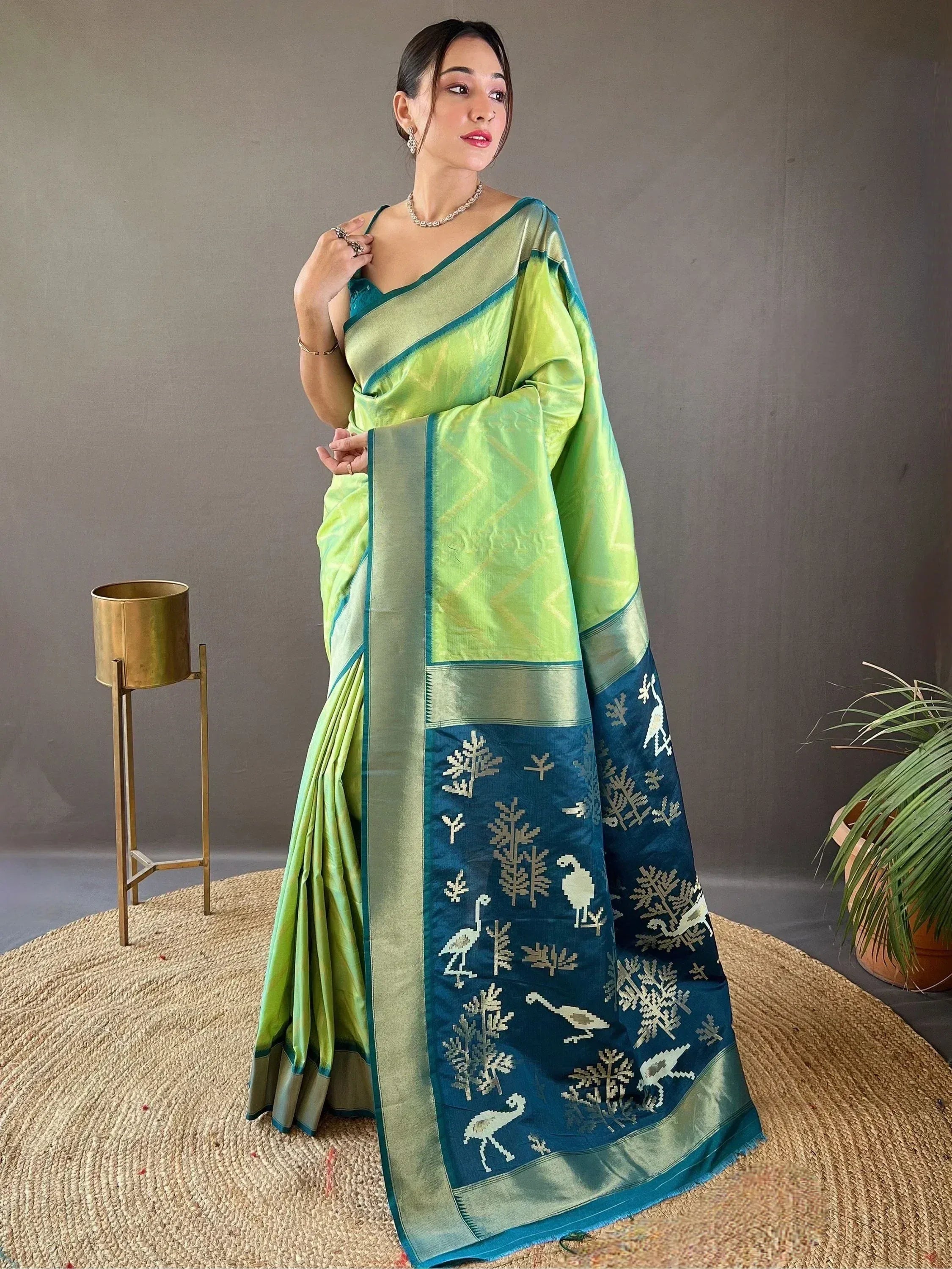Woman in vibrant green and blue ethnic saree with bird and tree motifs, perfect for Indian occasions.