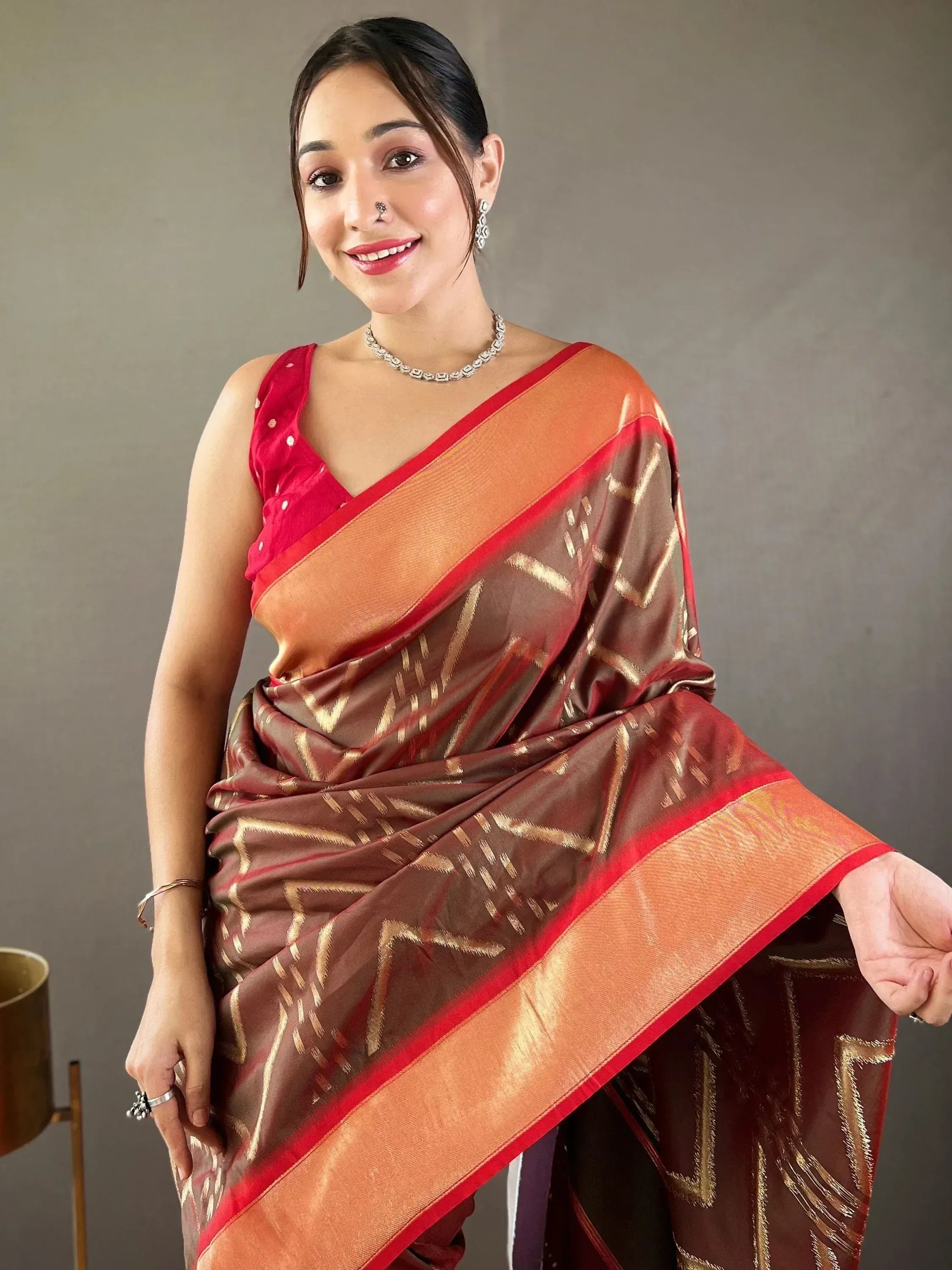 Woman in elegant brown and red saree with gold geometric patterns, paired with a red blouse and traditional jewelry