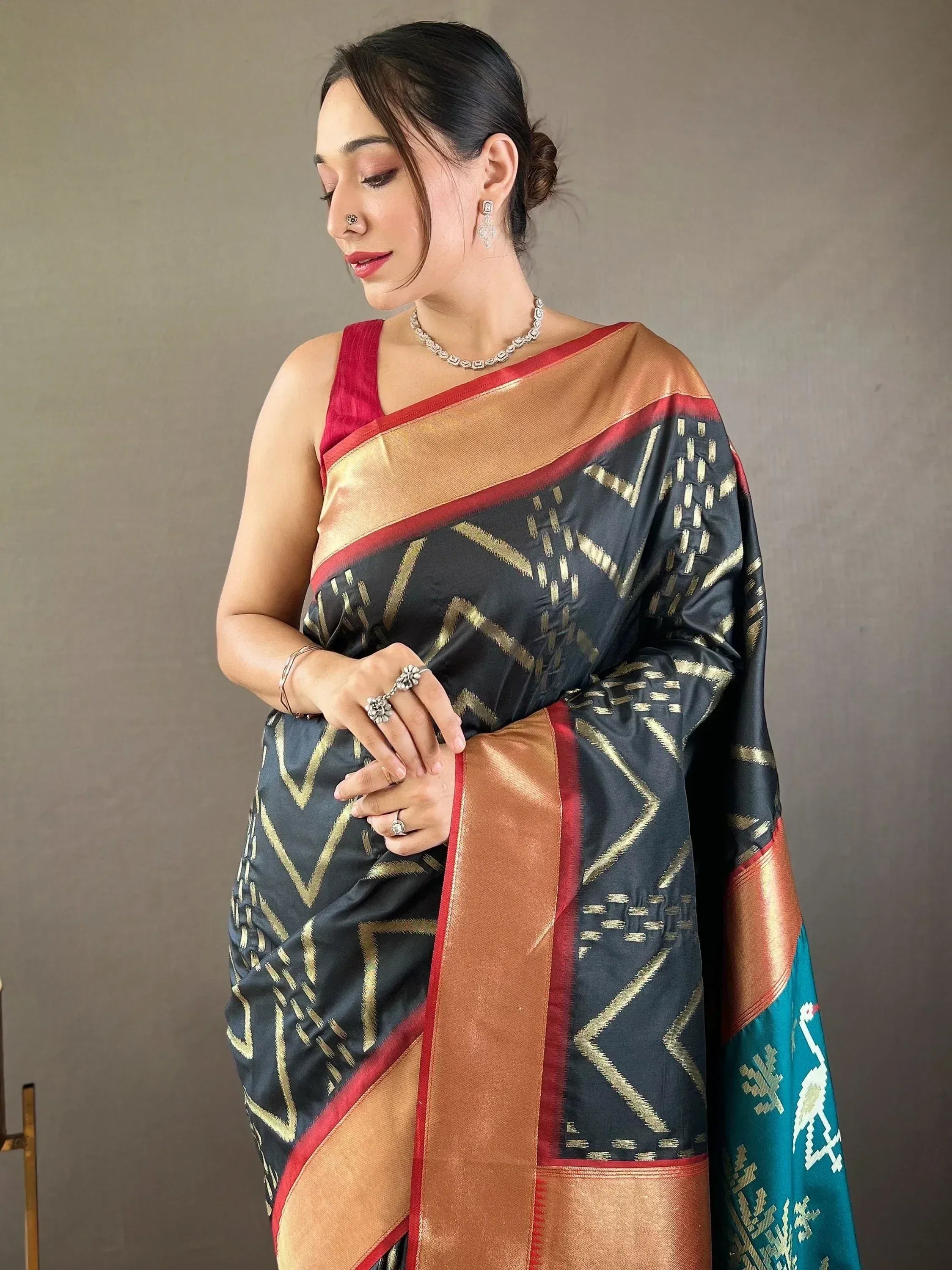 Black and gold geometric patterned saree with red and teal border, paired with red blouse and silver jewelry.