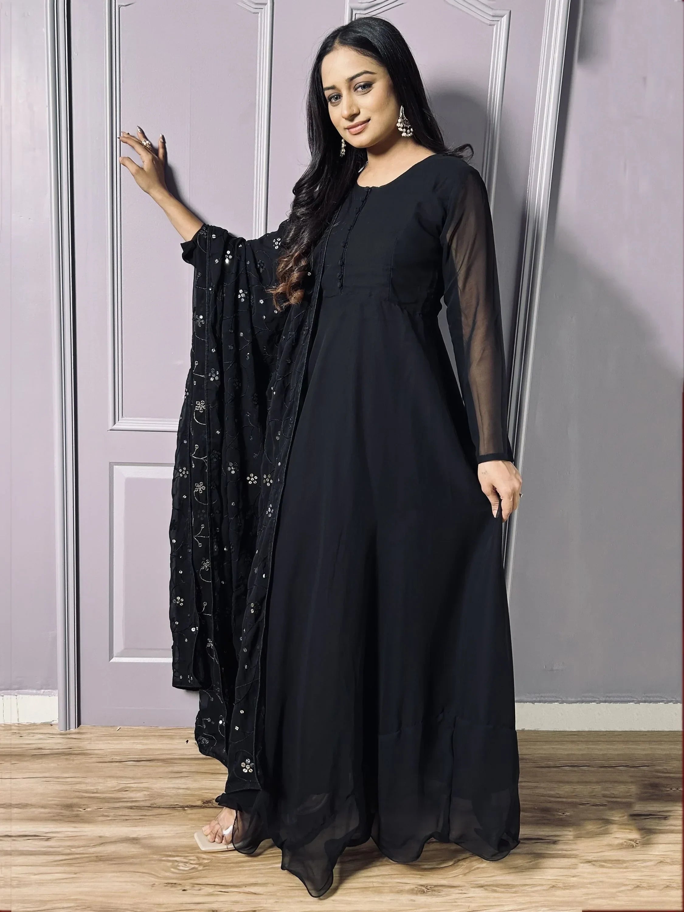 Woman in black Anarkali suit with embroidered dupatta and sheer sleeves, standing indoors