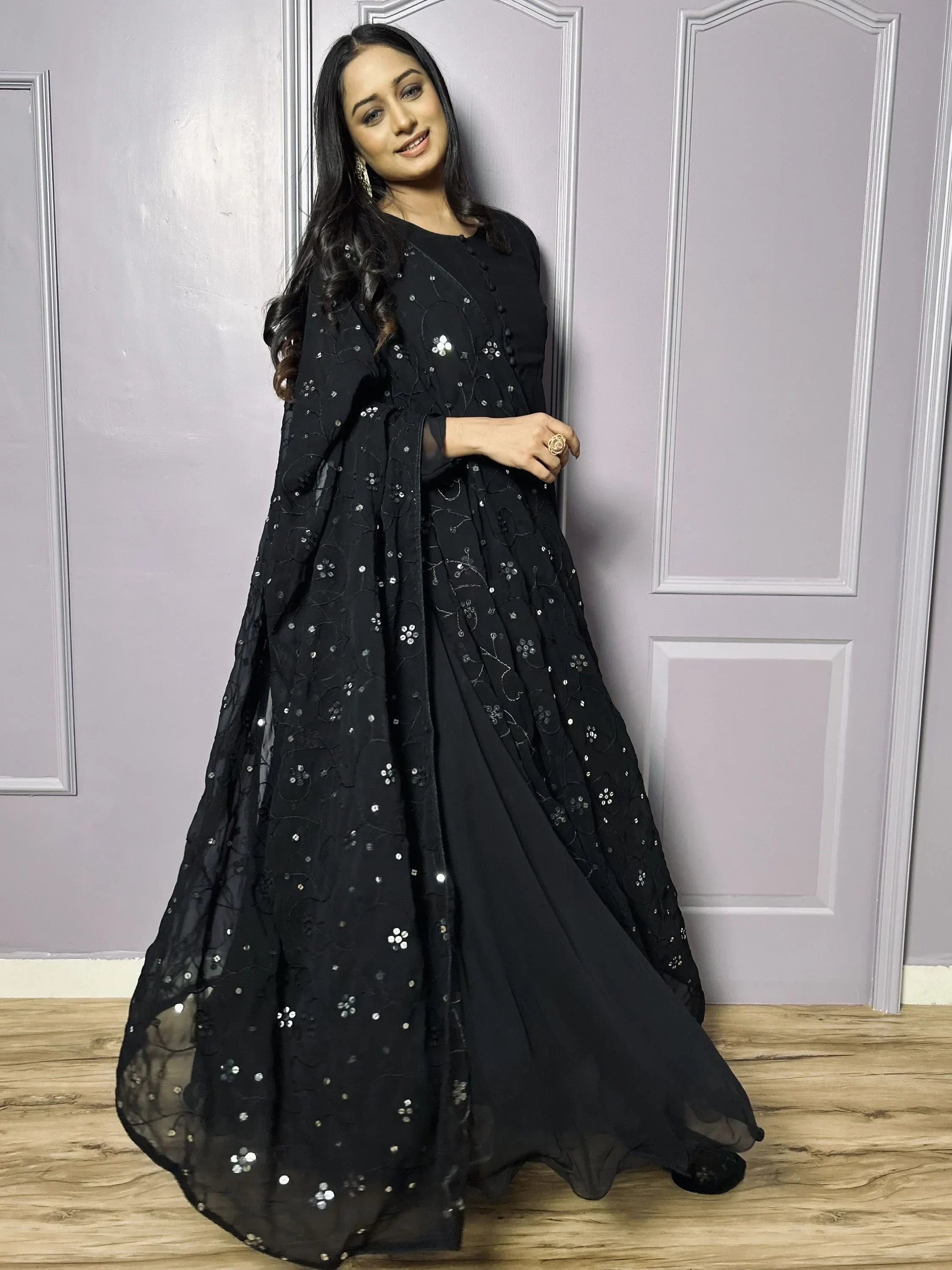 Woman in black embroidered ethnic gown with dupatta, standing indoors