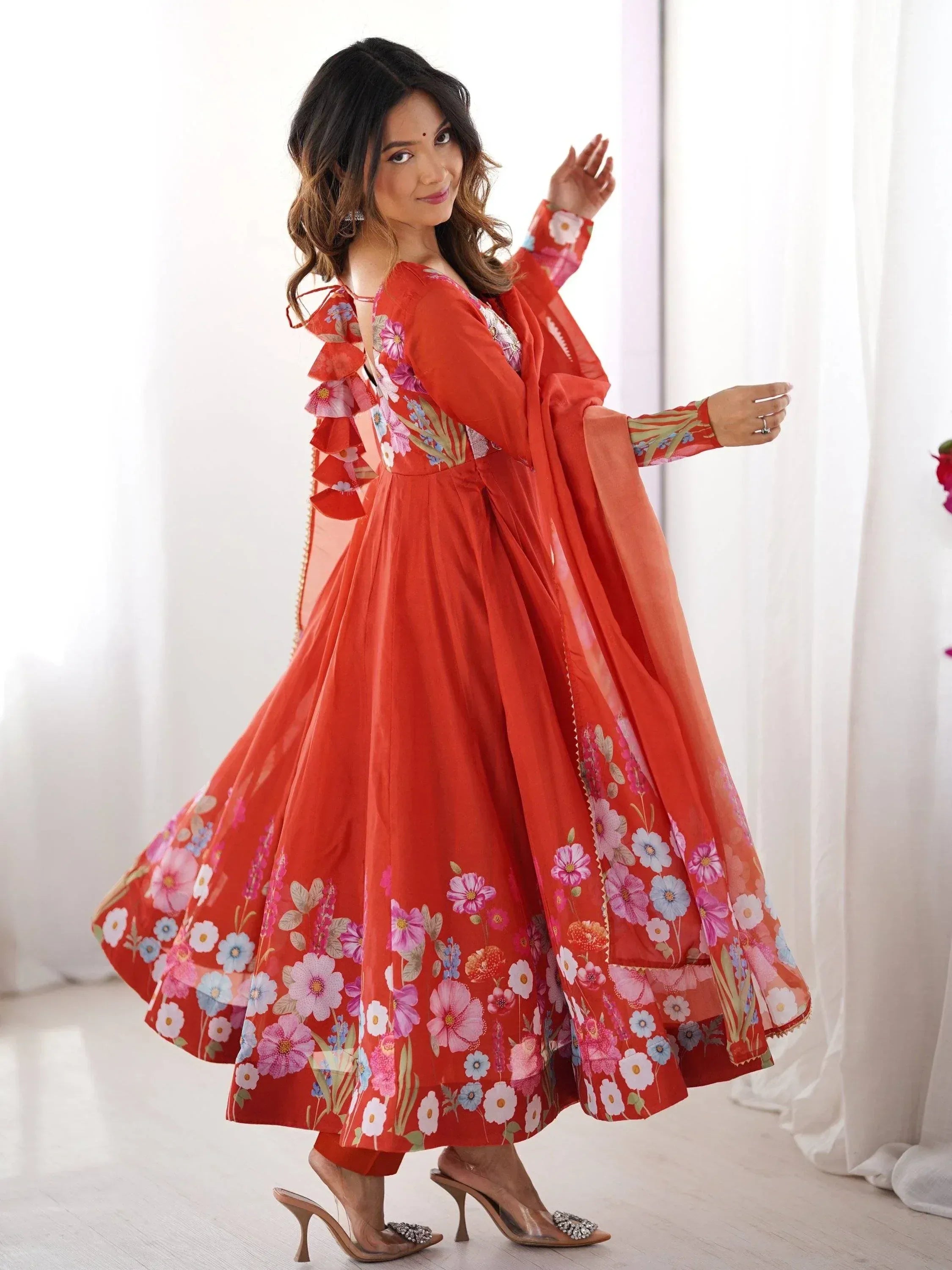 Woman in vibrant red floral print ethnic gown with ruffled sleeves and dupatta, perfect for festive occasions.