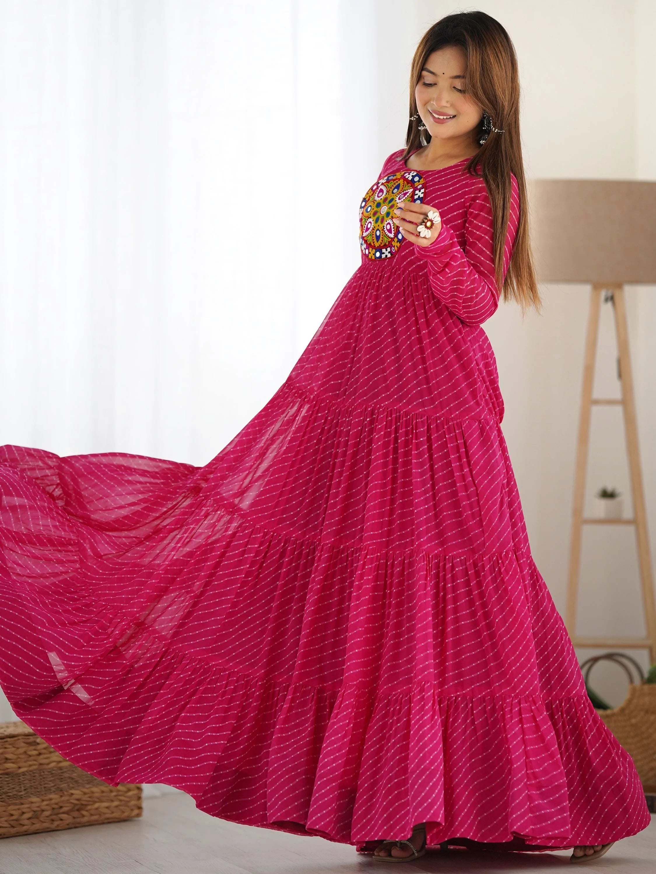 Woman wearing a vibrant pink ethnic gown with mirror work and striped pattern indoors