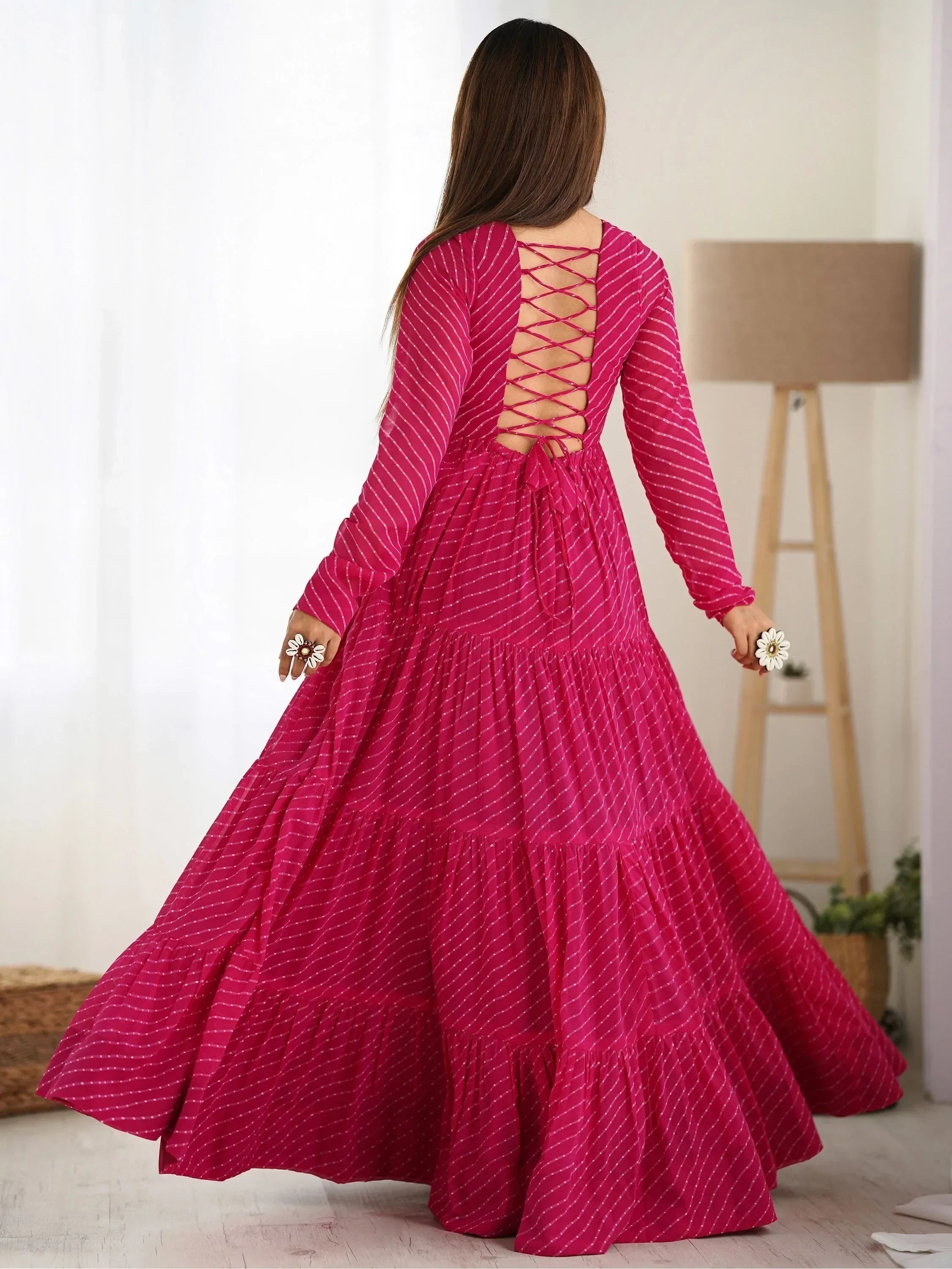Woman in a vibrant pink ethnic gown with crisscross back and flared skirt, indoor setting