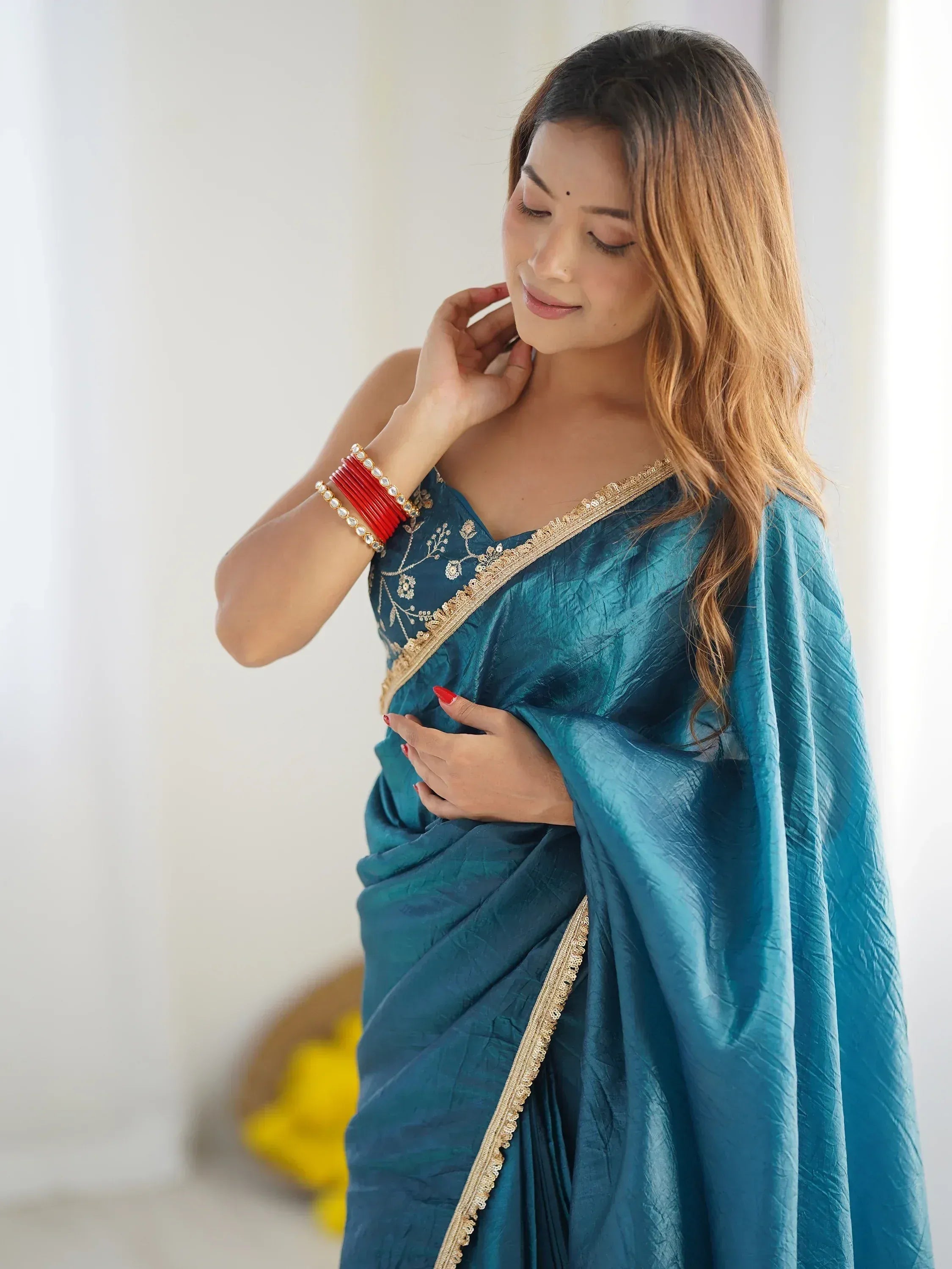 Woman in elegant teal saree with gold embroidery, red bangles, and subtle makeup