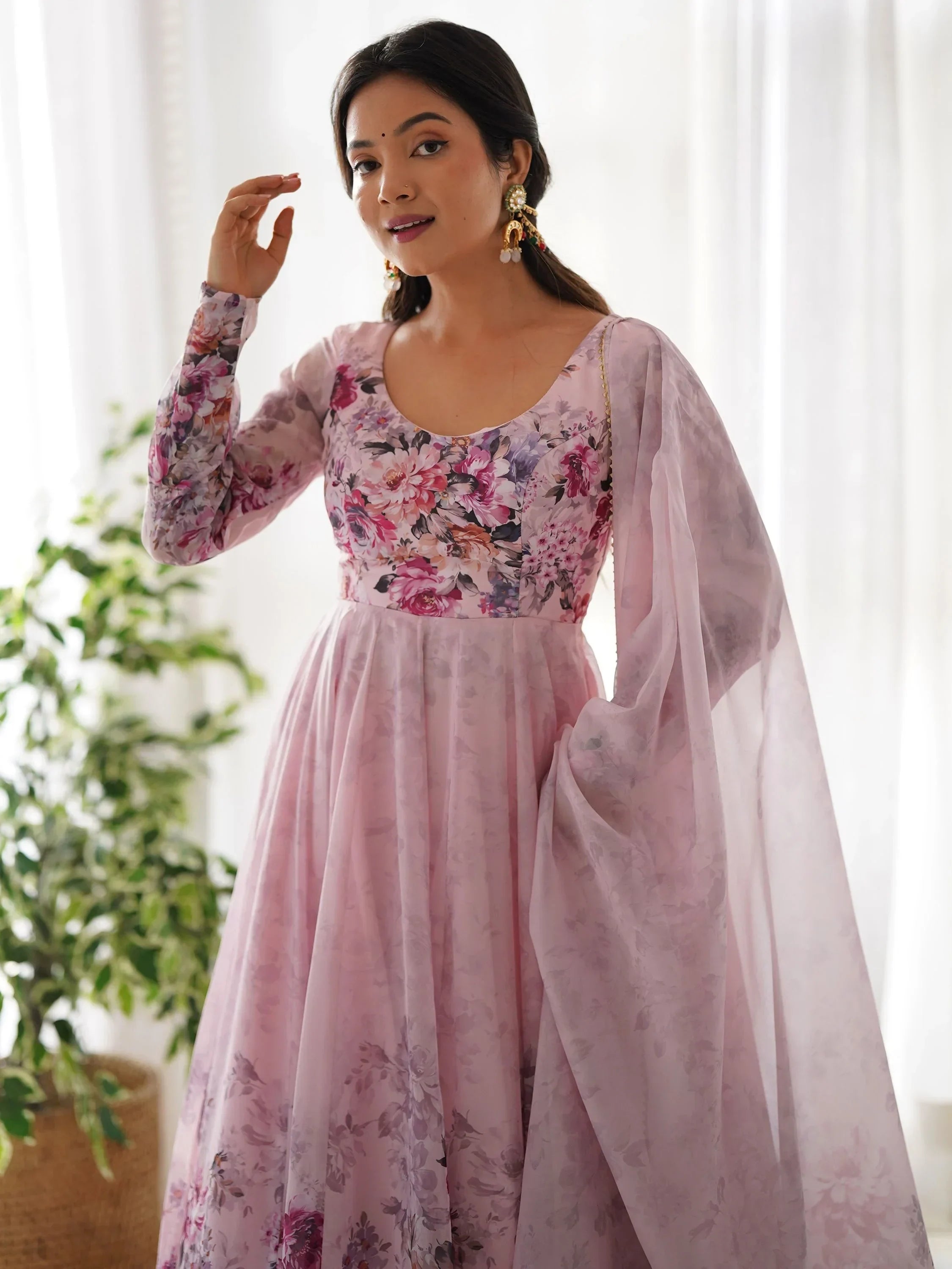 Woman wearing light pink floral ethnic gown with long sleeves and dupatta, indoor setting