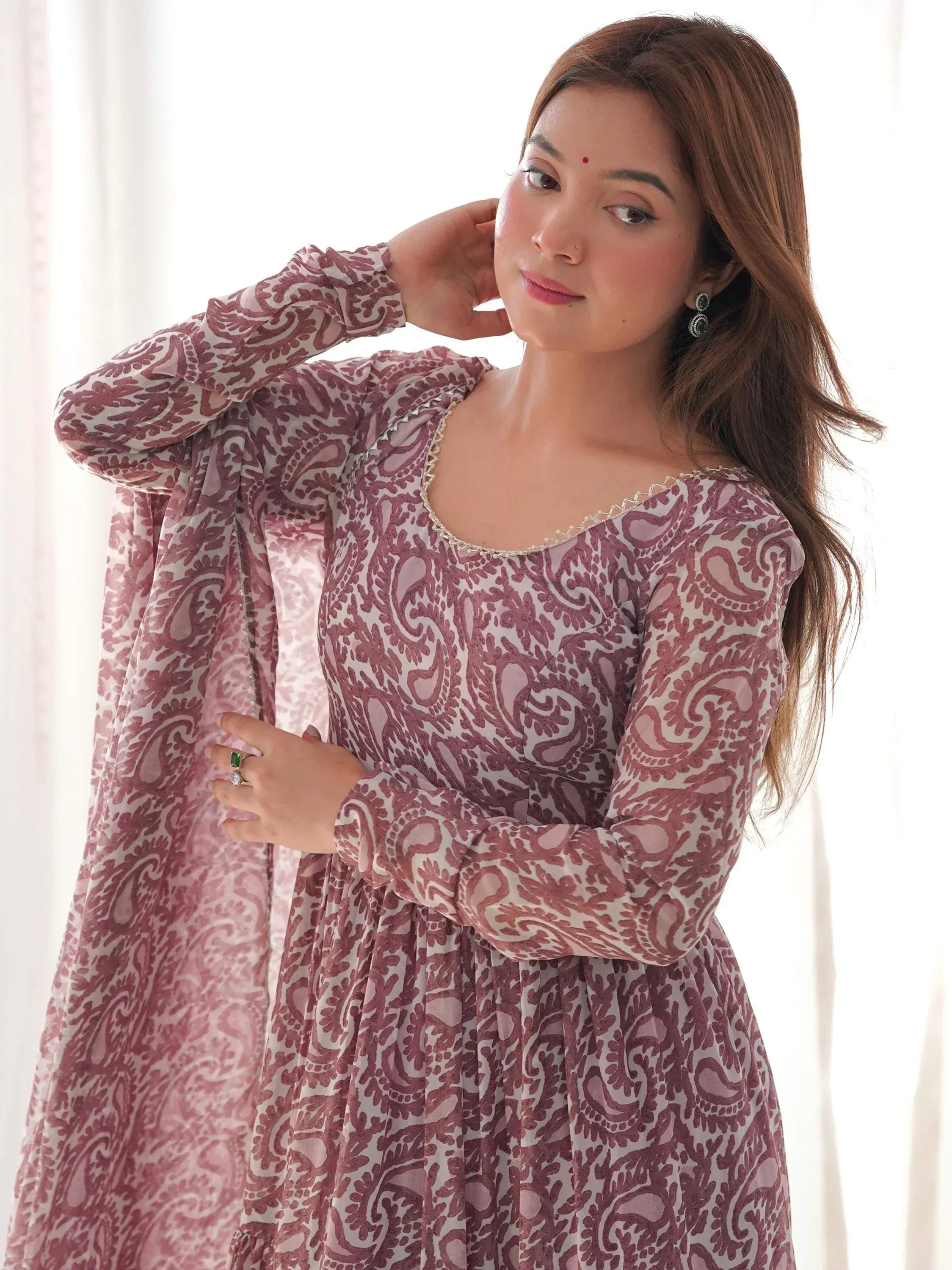 Woman in mauve printed ethnic gown with long sleeves, posing indoors in natural light