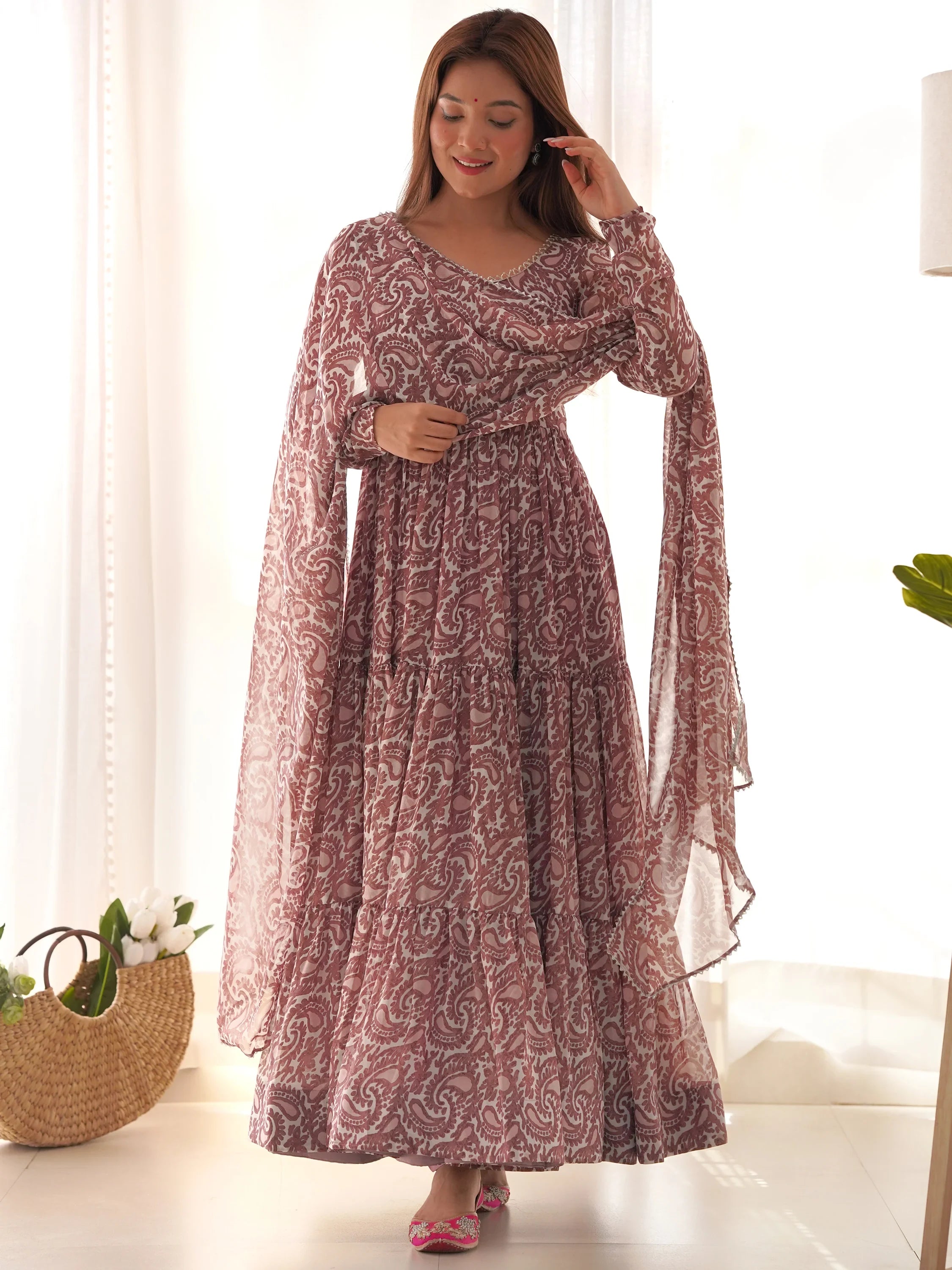 Woman in a pink paisley printed ethnic gown with dupatta, standing indoors