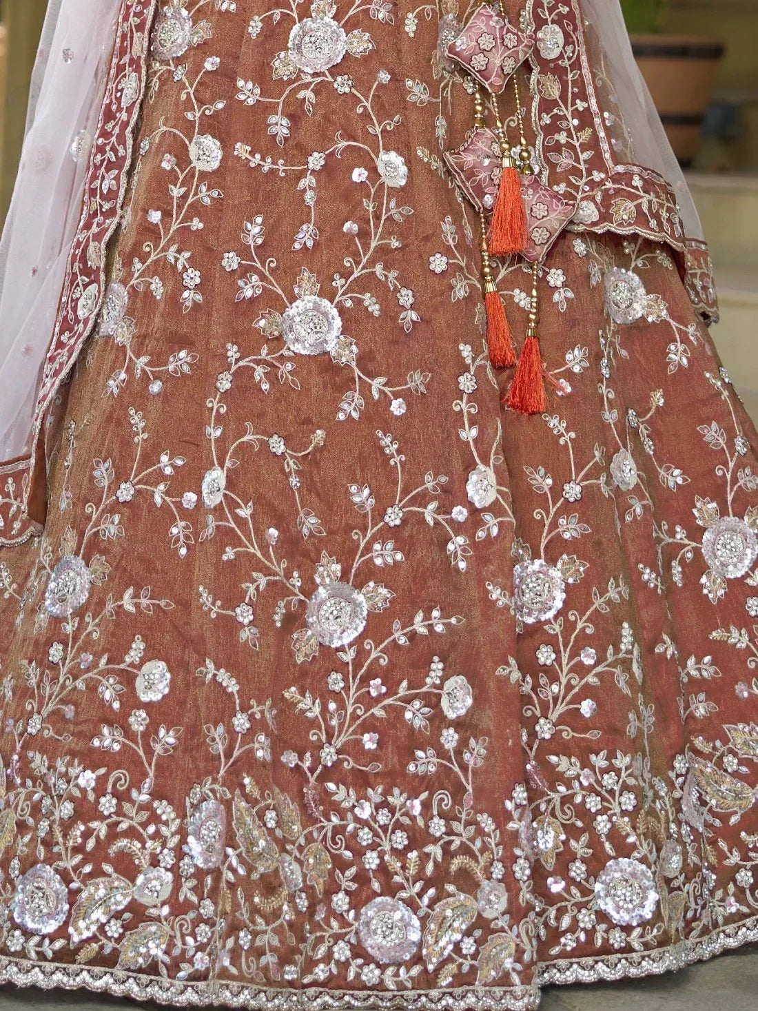 Brown designer lehenga with silver floral embroidery and orange tassels, perfect for Indian weddings