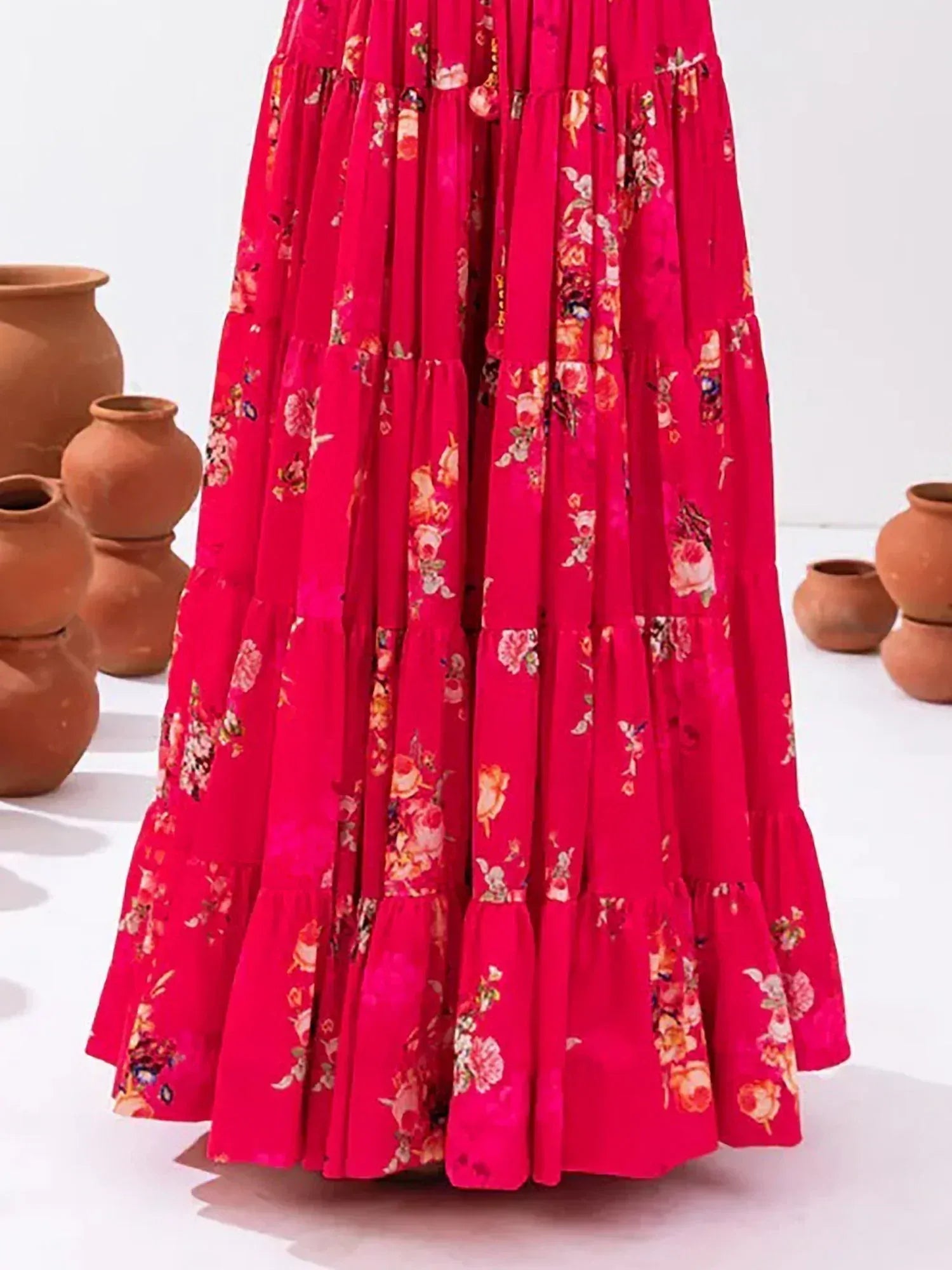 Vibrant pink floral tiered ethnic gown with ruffled layers, styled with clay pots for traditional Indian wear.