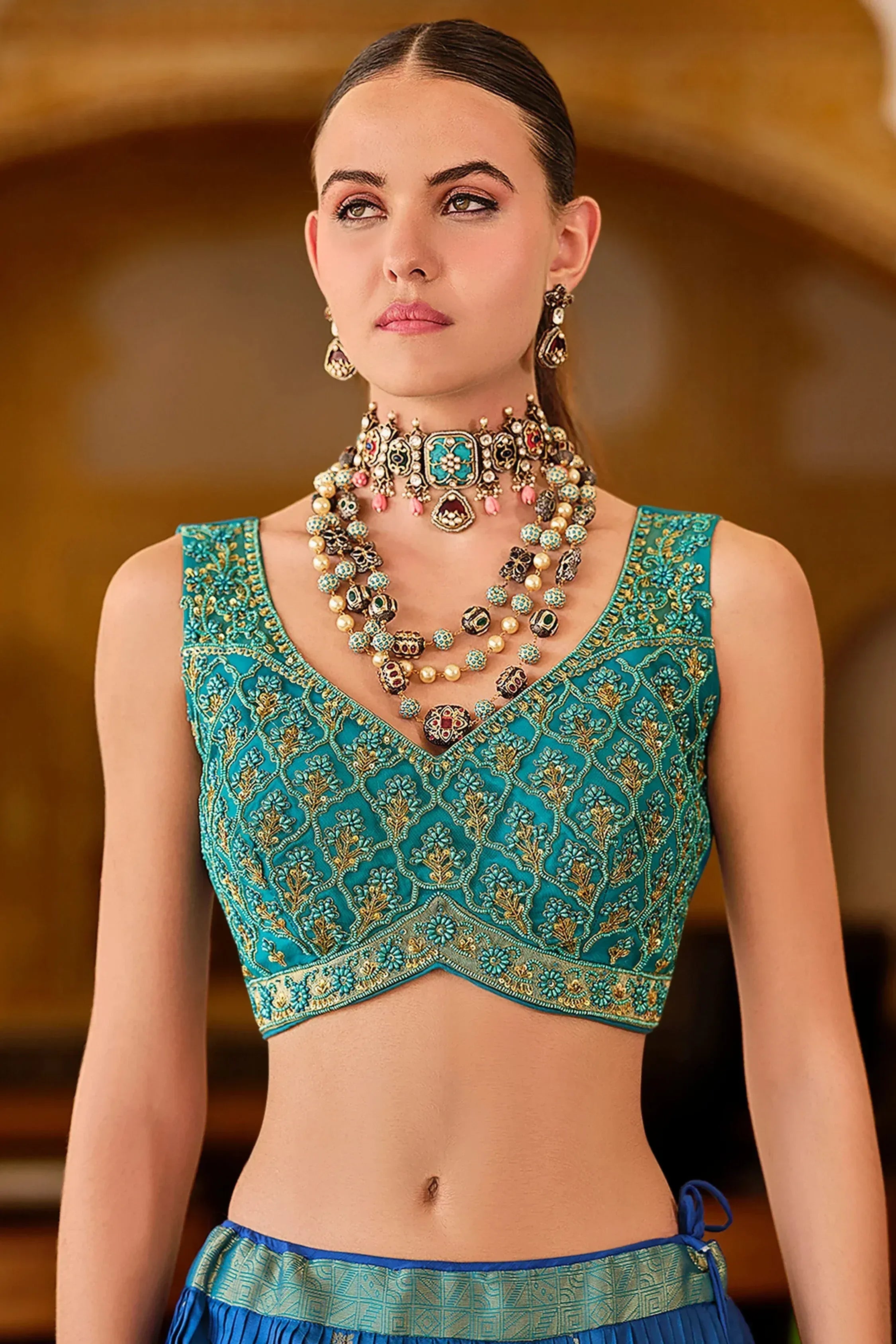 Teal embroidered blouse with gold detailing, paired with traditional Indian jewelry for ethnic wear