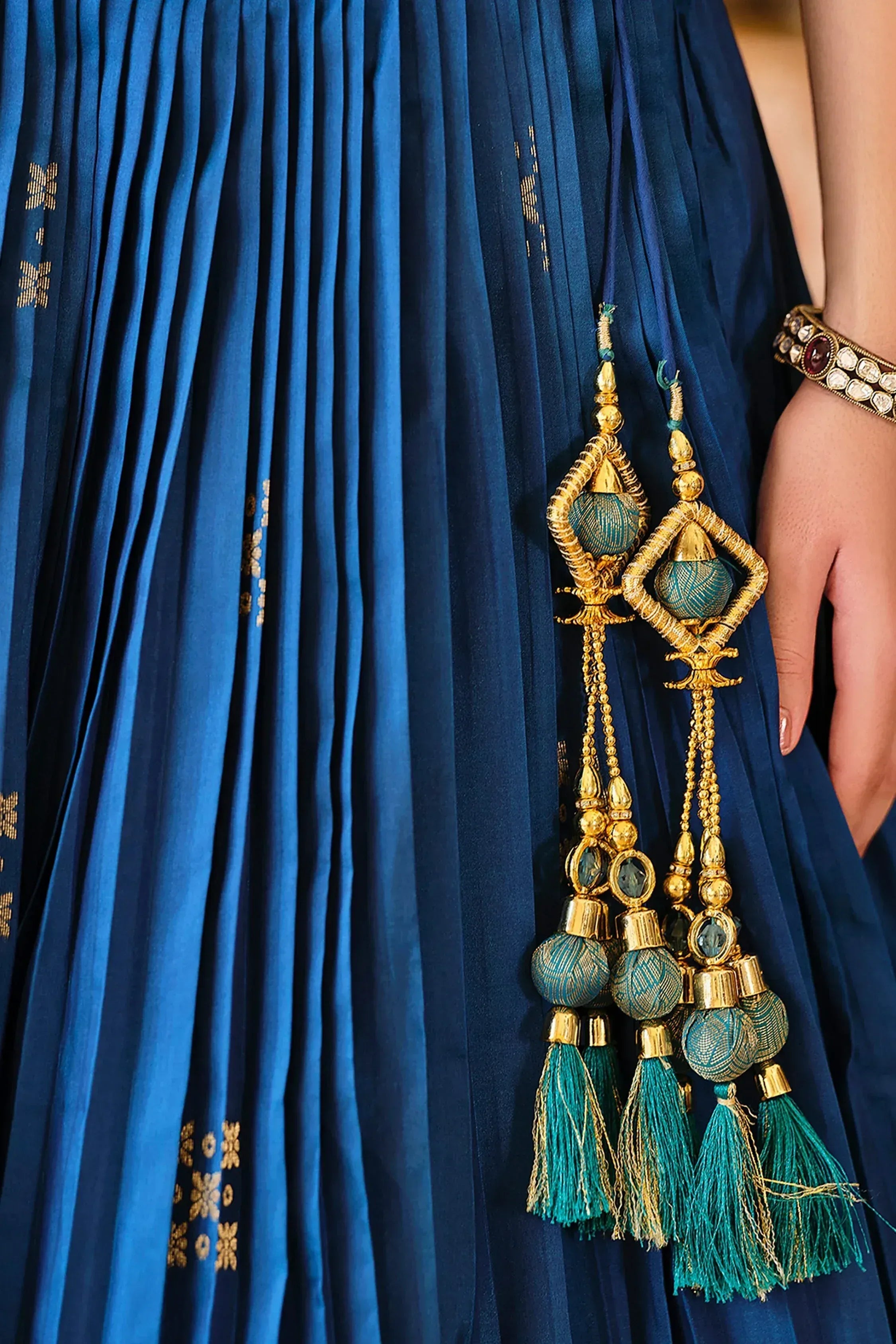 Royal blue pleated ethnic gown with gold embroidery and tassel detailing, paired with traditional jewelry.