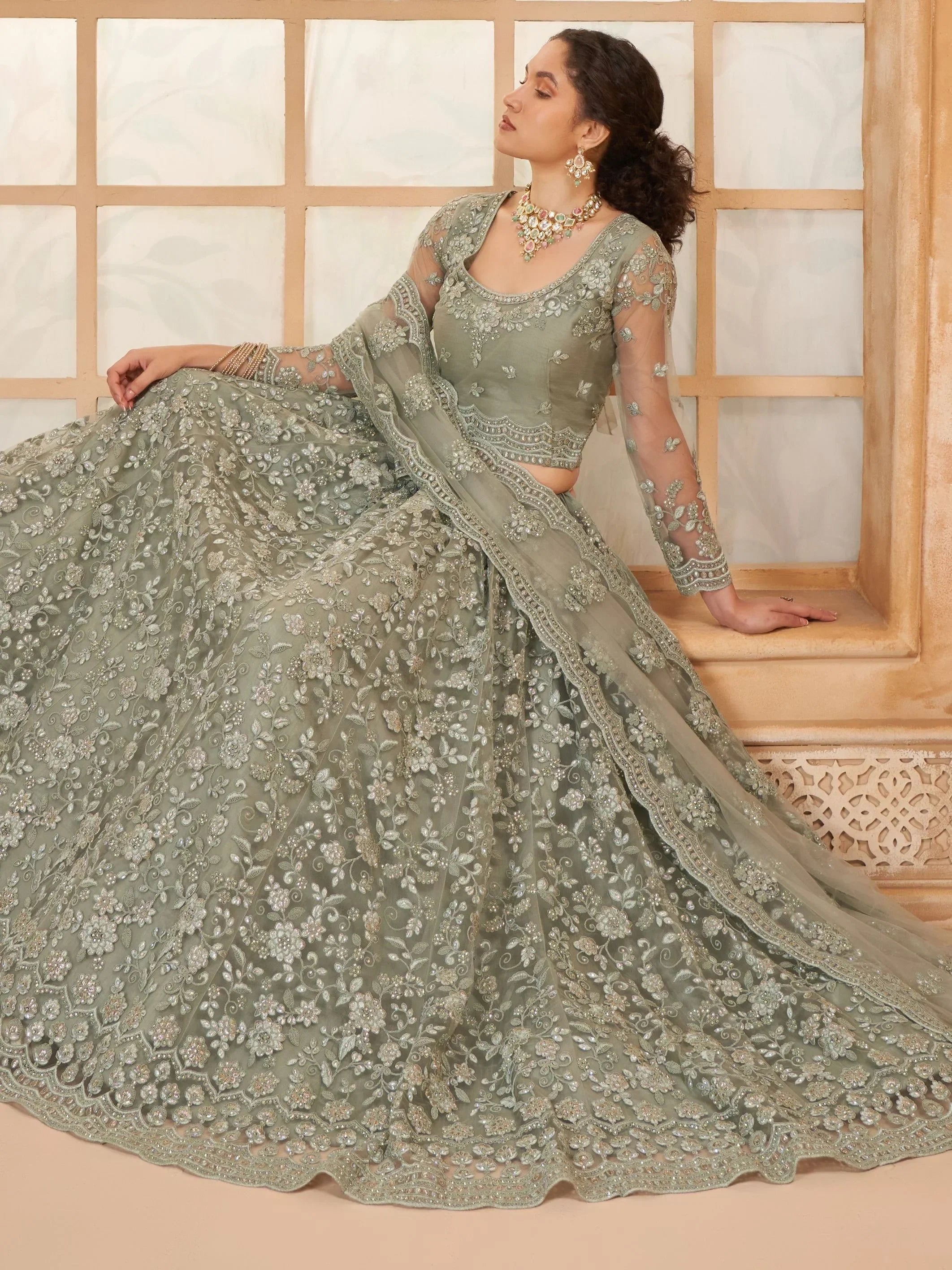 Elegant sage green lehenga choli with intricate floral embroidery and sheer sleeves, perfect for Indian weddings.