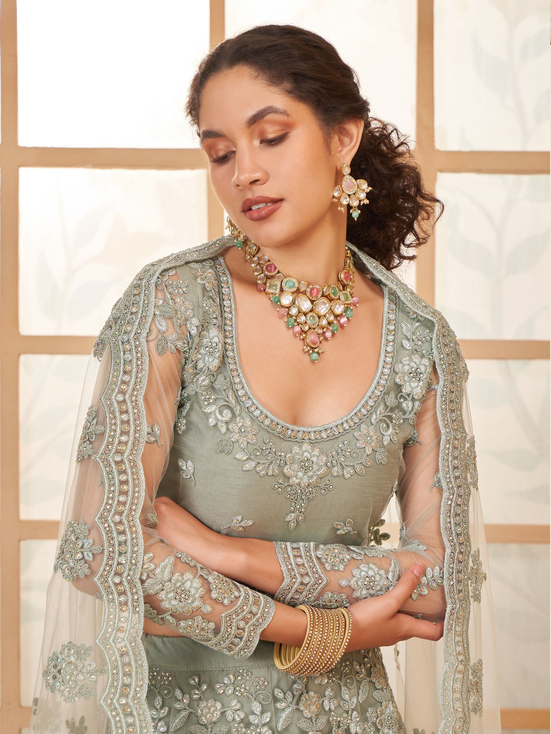 Elegant sage green embroidered lehenga choli with sheer cape, paired with traditional jewelry for Indian ethnic wear.