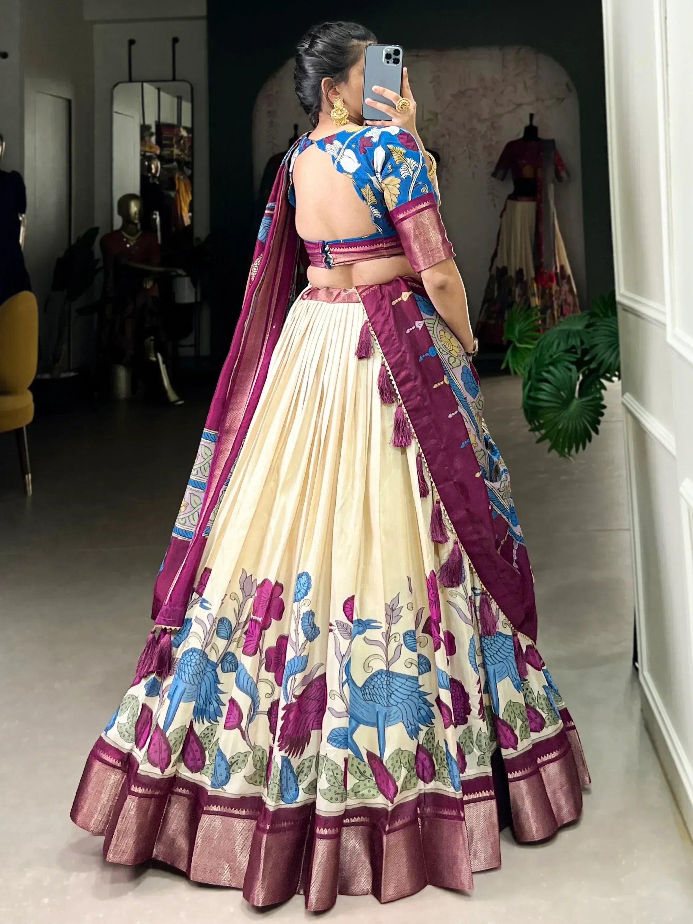 Woman in floral print lehenga choli with blue and maroon dupatta, taking mirror selfie in boutique