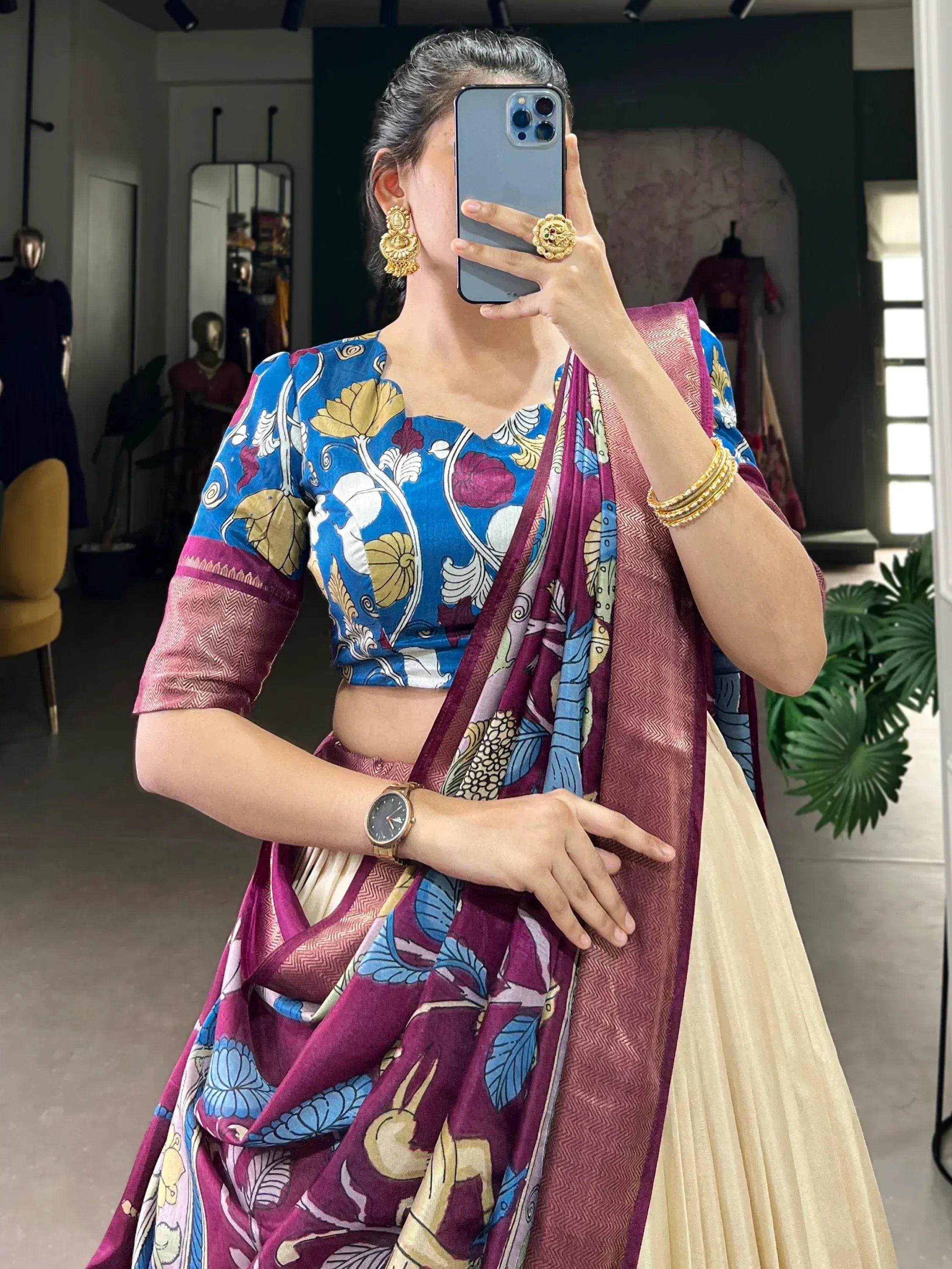 Woman in blue floral blouse & maroon printed saree, gold jewelry, mirror selfie at boutique