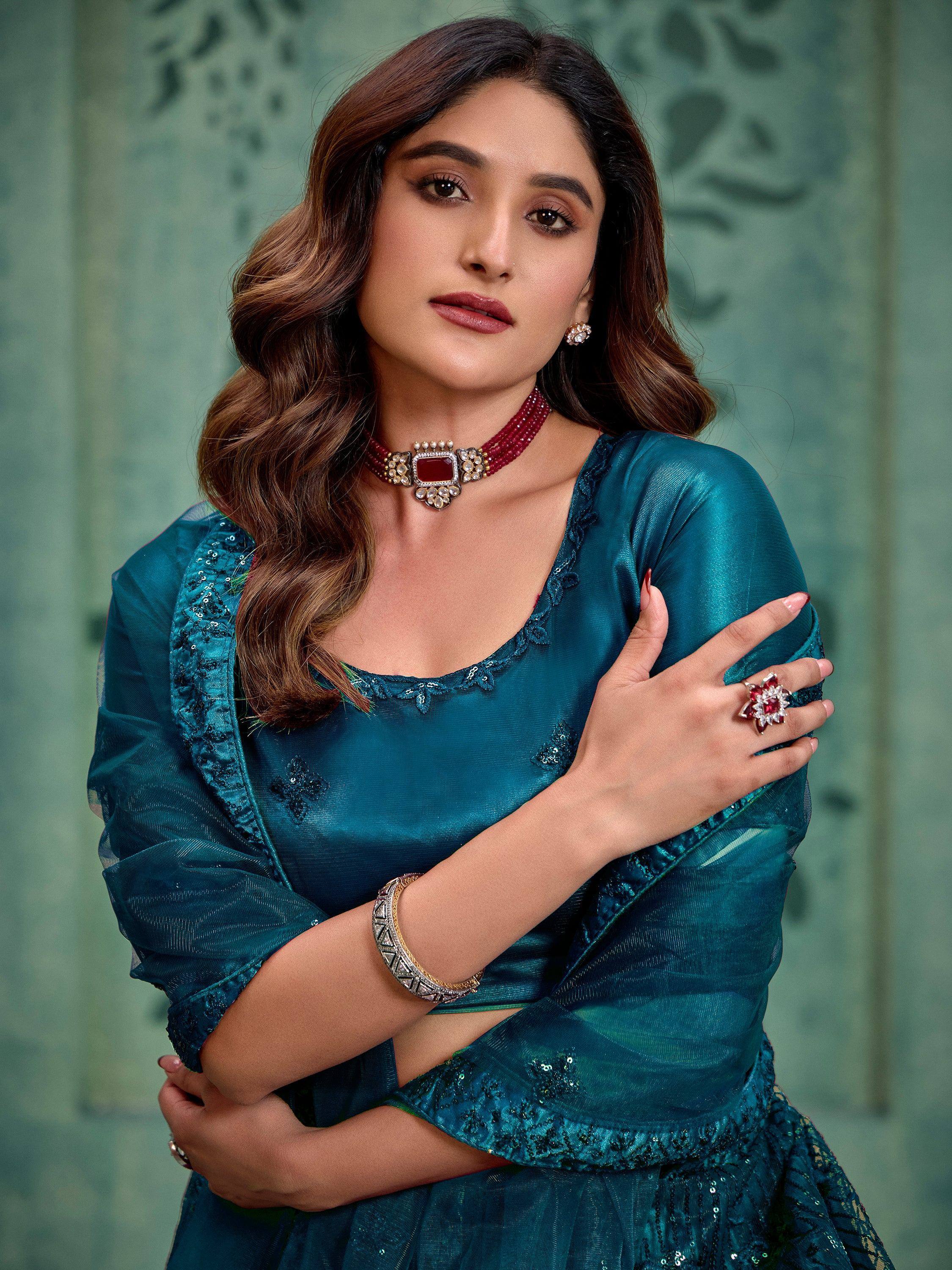 Teal ethnic gown with sequin detailing, paired with red gemstone jewelry for festive occasions