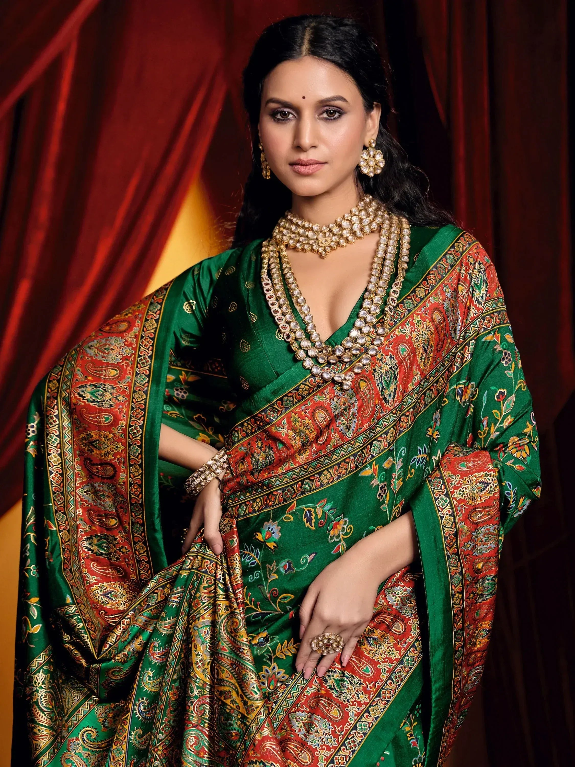 Elegant green and red printed saree with intricate paisley design, paired with traditional jewelry for festive occasions.