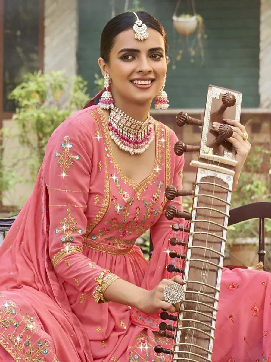 Woman in pink embroidered ethnic gown holding sitar, adorned with traditional jewelry