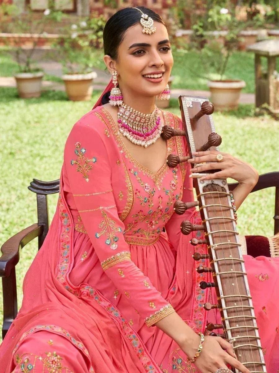 Woman in pink embroidered ethnic gown holding sitar, adorned with traditional jewelry