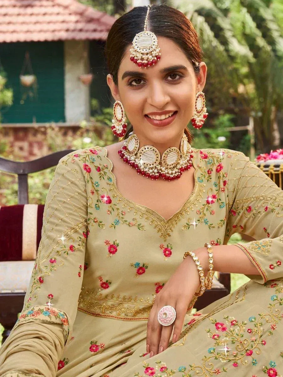 Woman in floral embroidered beige salwar kameez with gold detailing and traditional jewelry