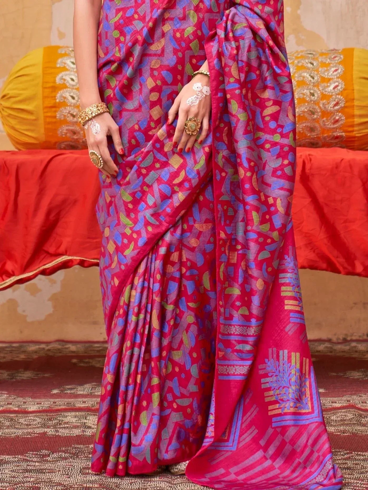 Vibrant pink and blue printed saree with geometric patterns, styled with gold jewelry for ethnic wear.