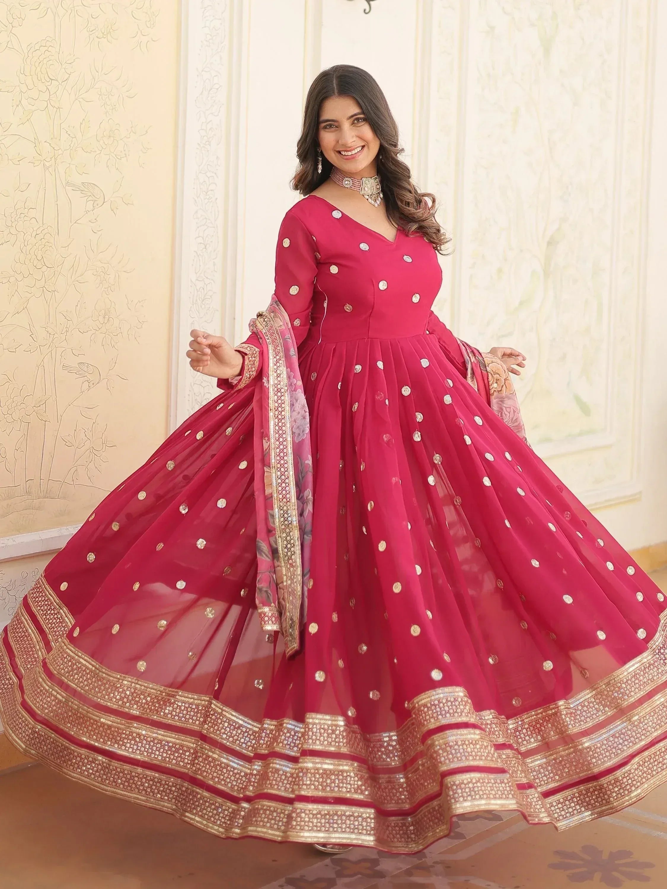 Woman in vibrant pink Indian ethnic anarkali gown with gold embroidery and floral dupatta, perfect for festive occasions.