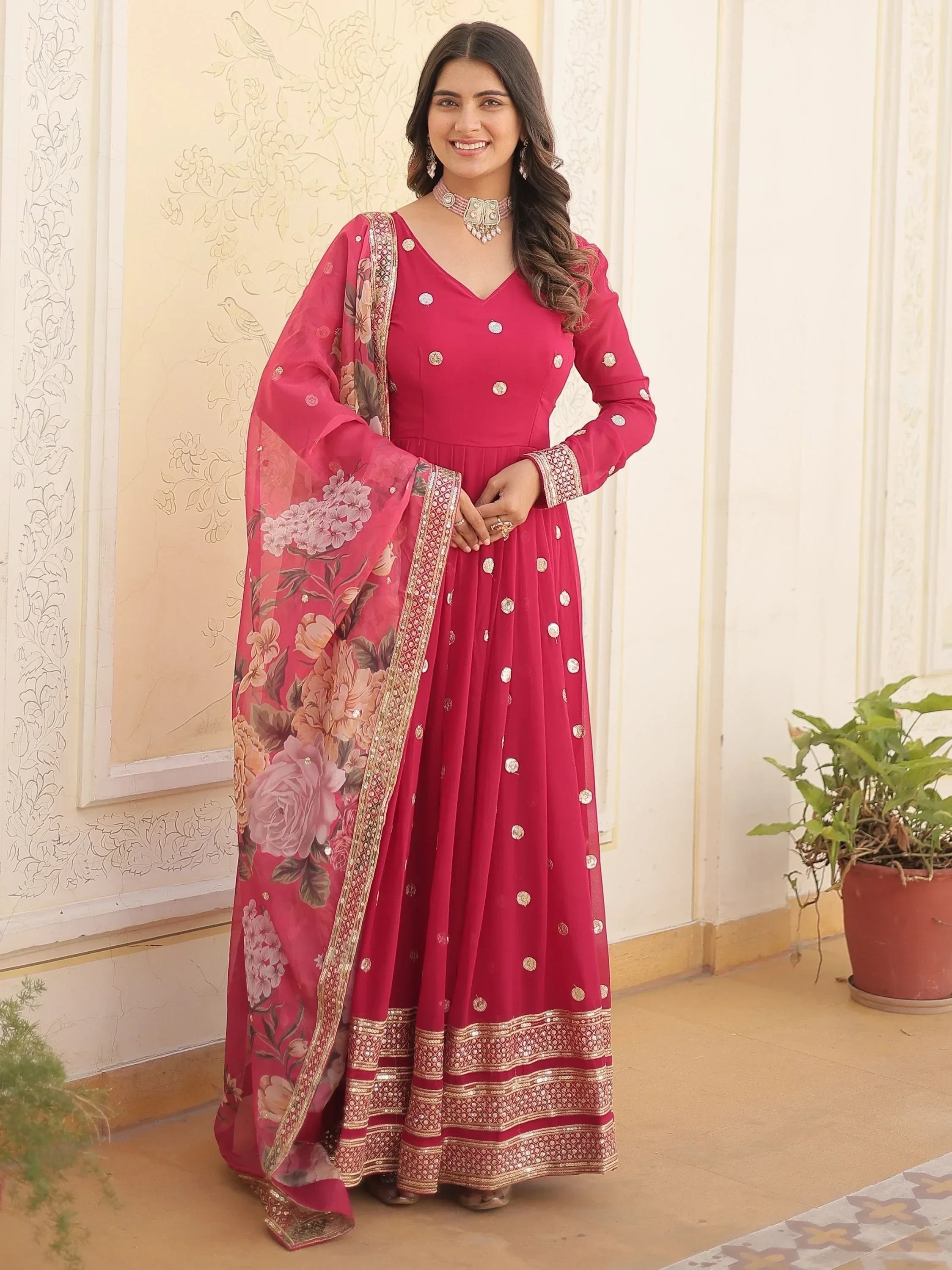 Woman in pink embroidered Anarkali suit with floral dupatta, gold details, and jewelry