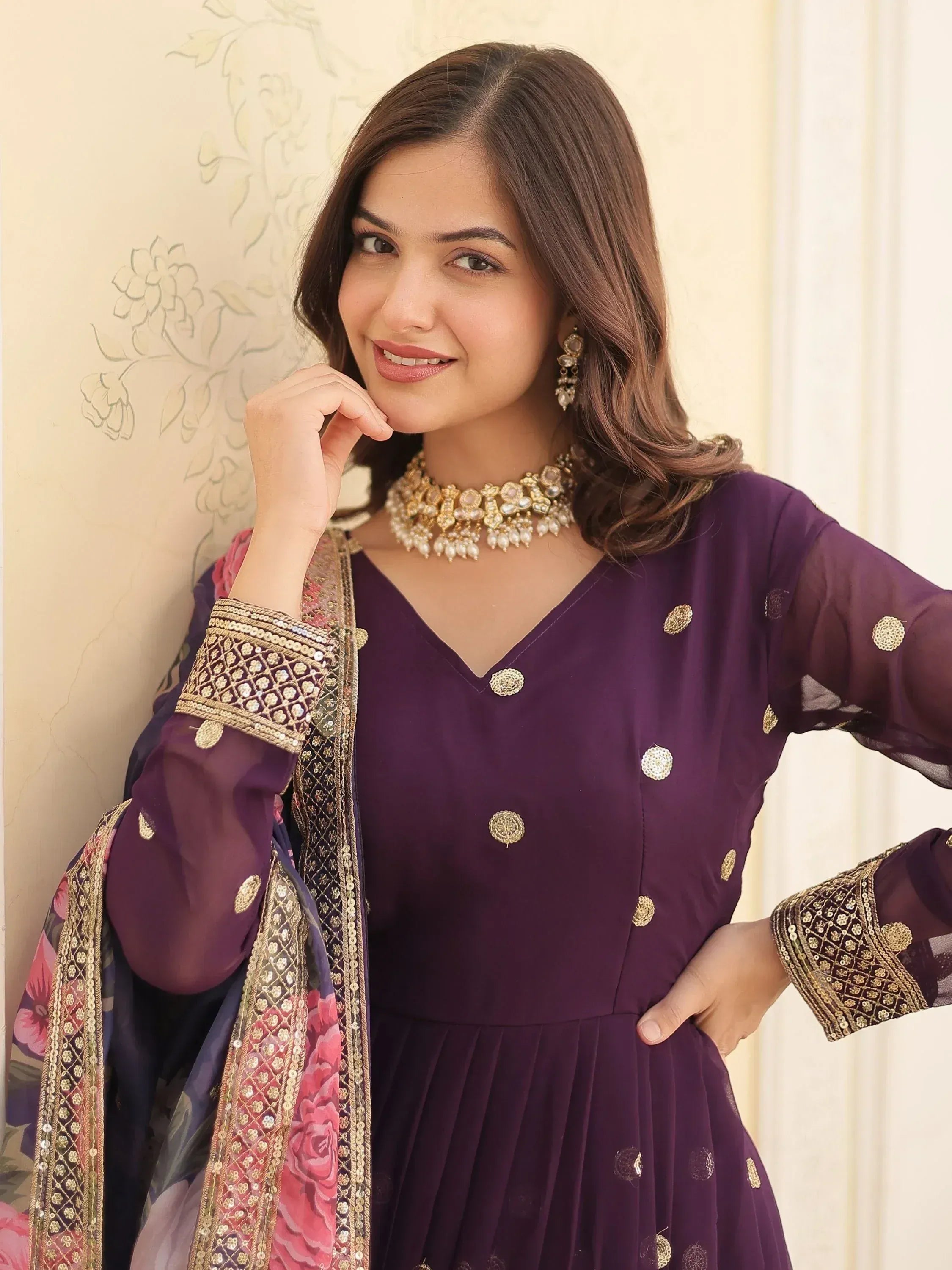 Purple ethnic gown with gold embroidery and floral dupatta, styled with traditional jewelry for festive occasions.