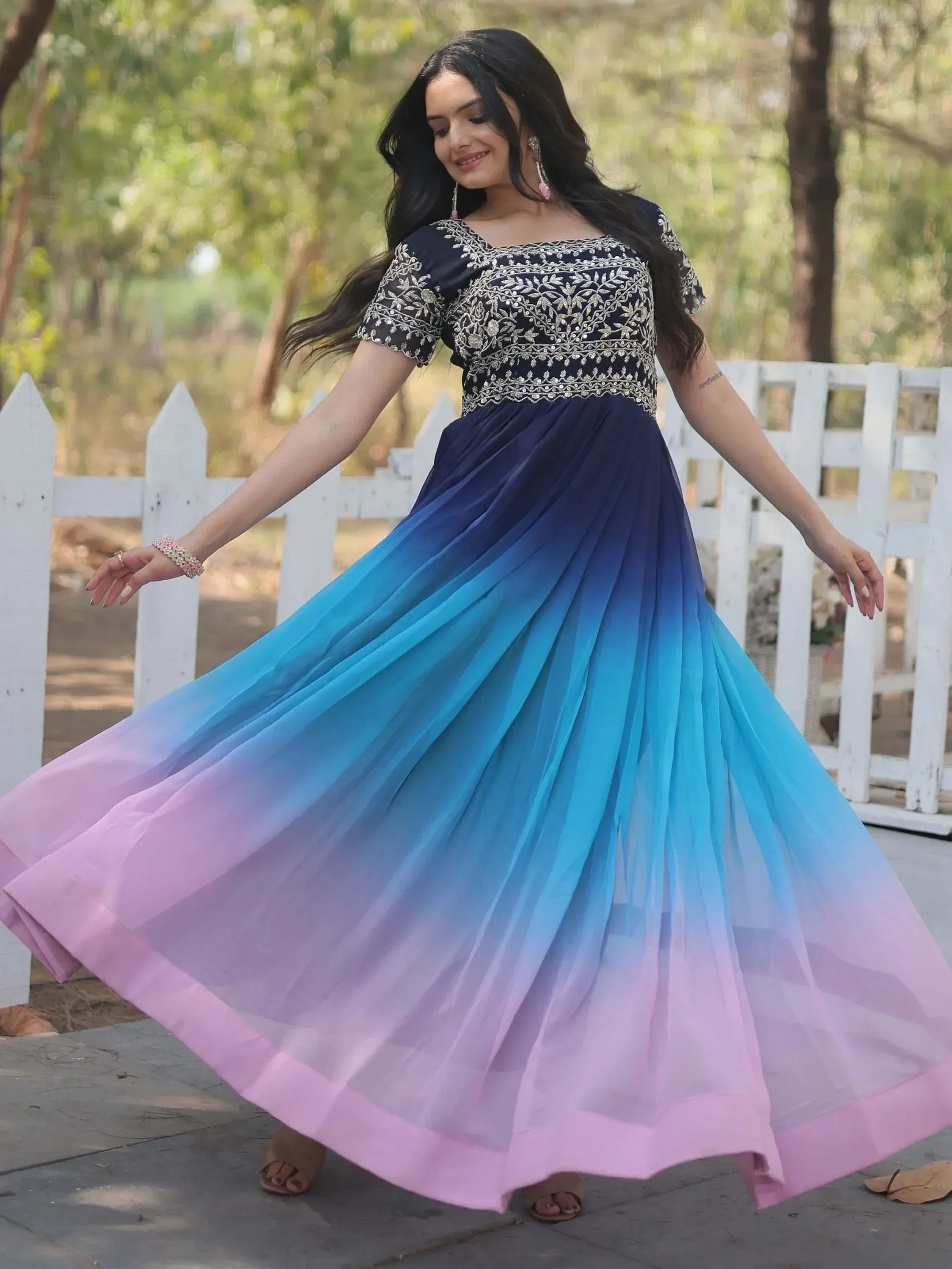 Woman twirling in a navy blue to pink ombre ethnic gown with gold embroidery, perfect for Indian occasions.