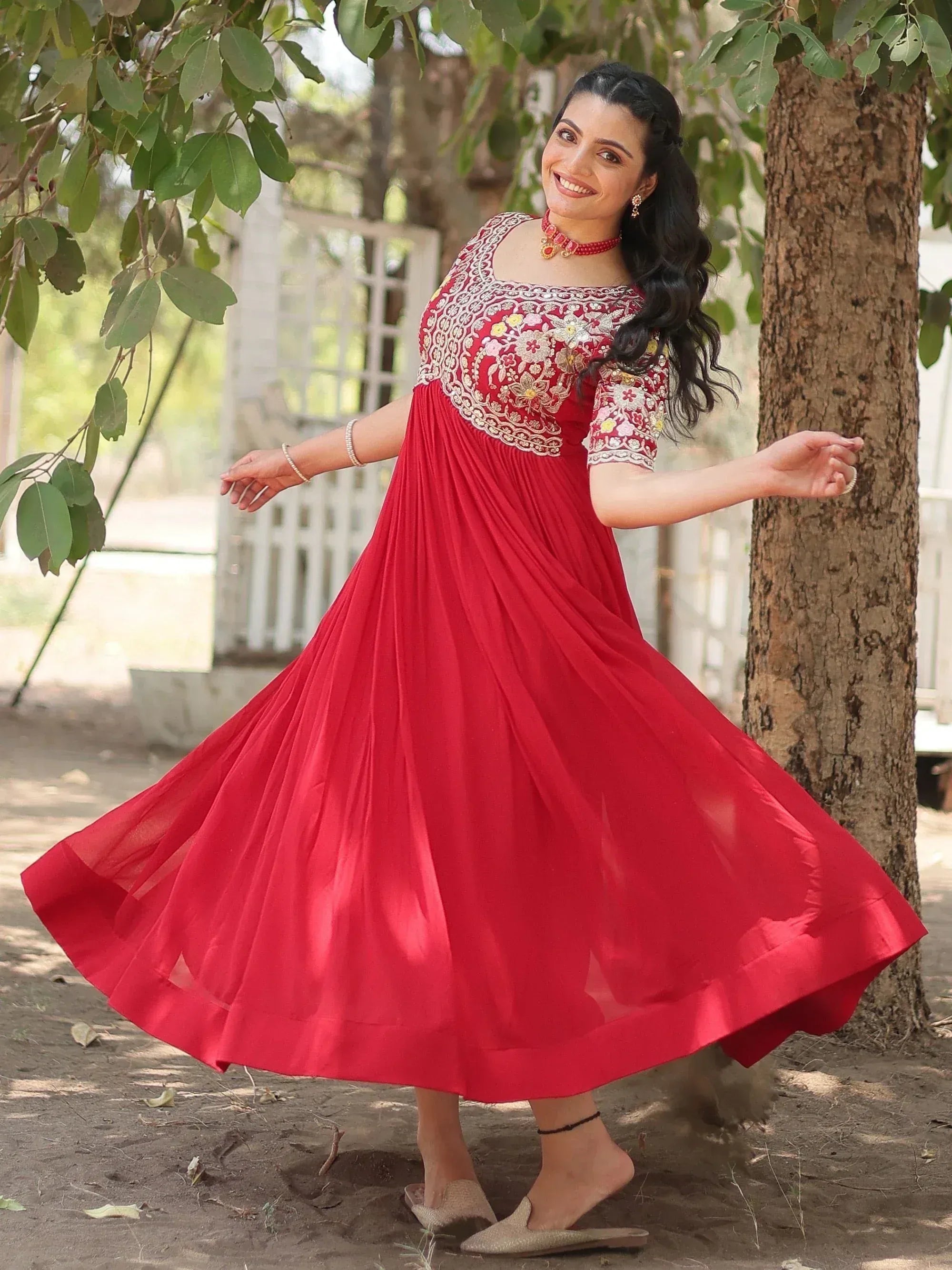 Woman in red ethnic gown with floral embroidery, twirling under tree