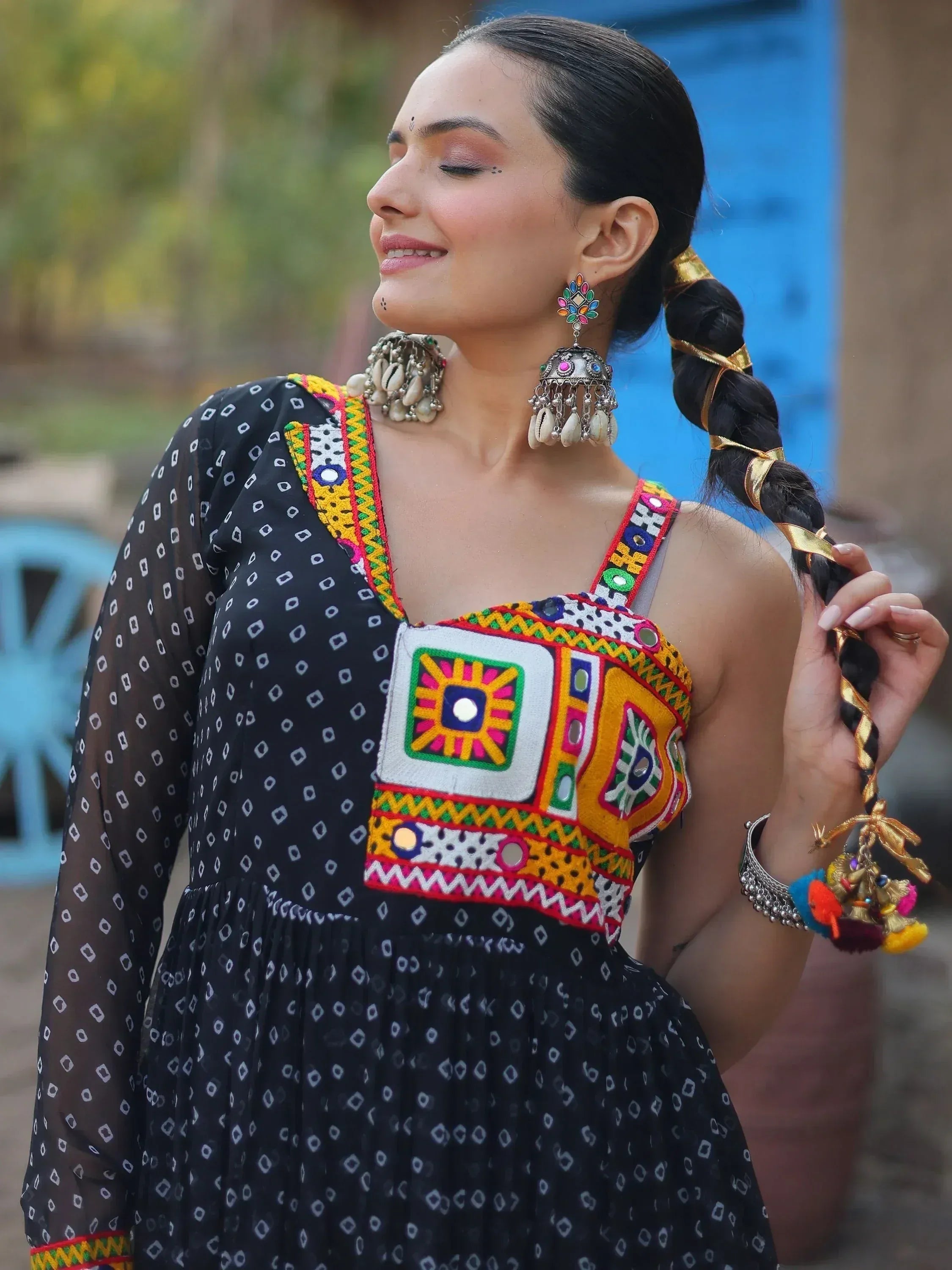 Woman in black ethnic dress with colorful mirror embroidery, jhumka earrings, and braided hair