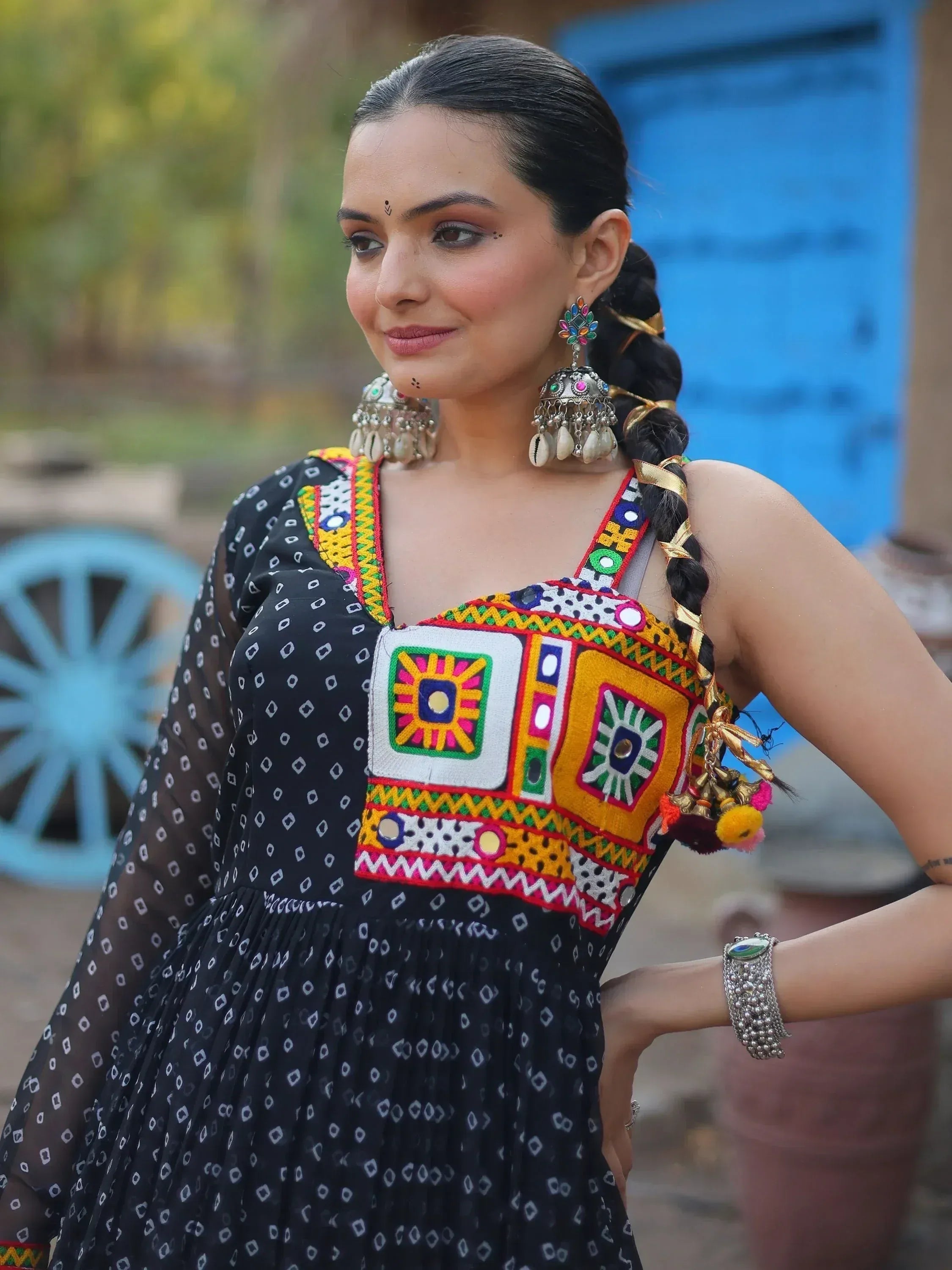 Woman in black ethnic gown with colorful mirror embroidery, jhumka earrings, and braided hair