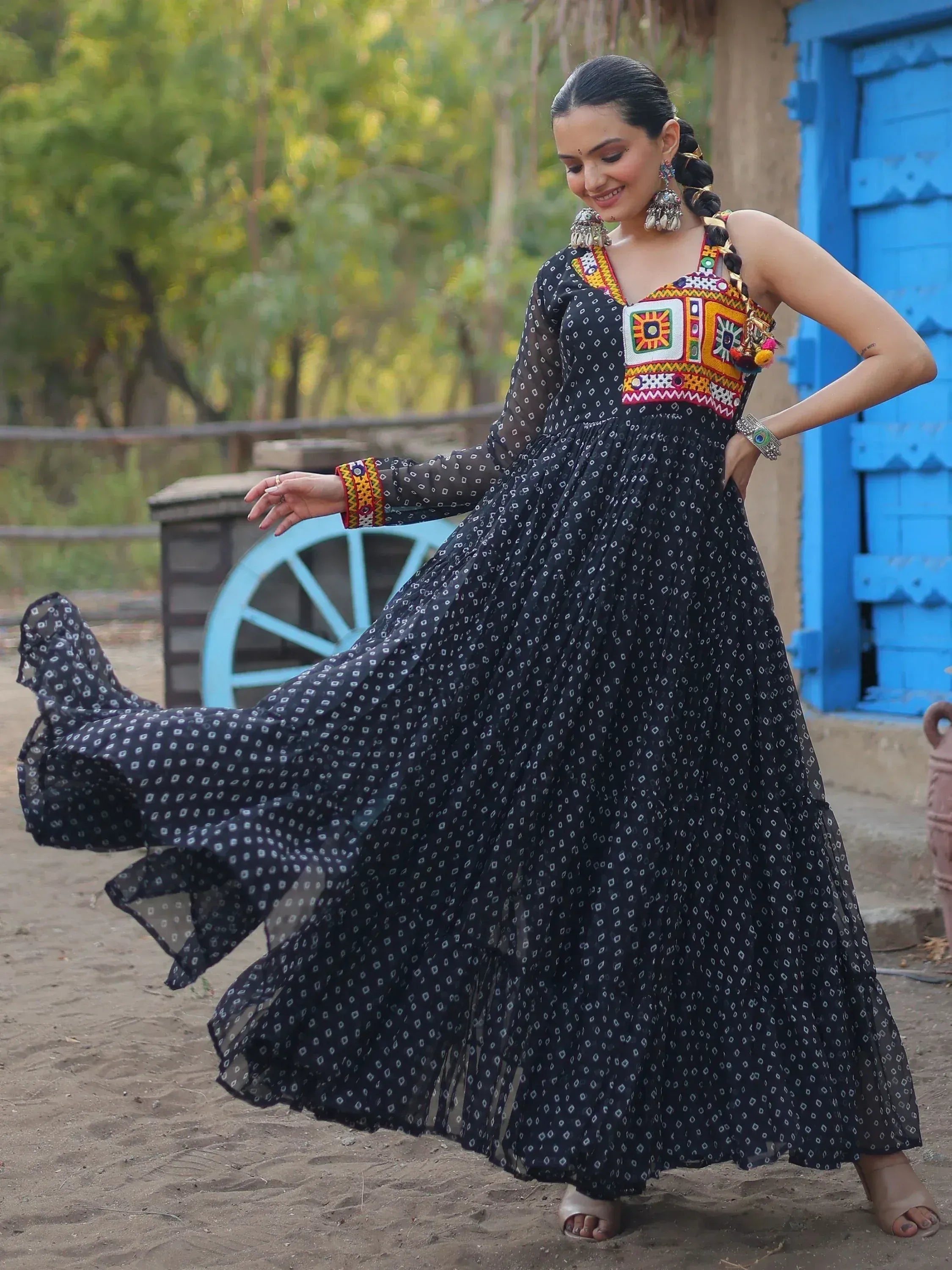 Woman in black ethnic gown with colorful embroidery, twirling outdoors near blue door